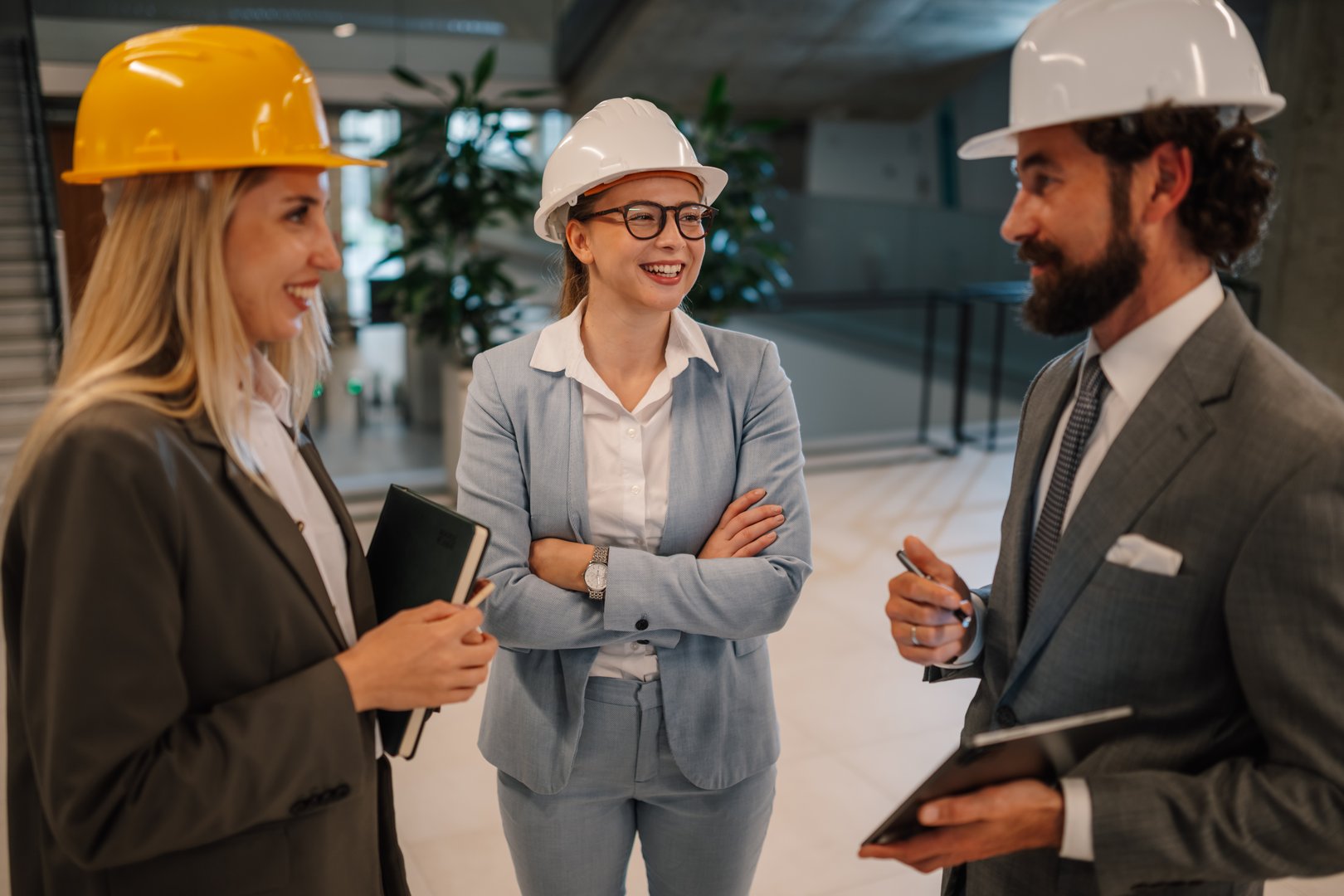Three engineers wearing suits and hardhats are discussing a project inside a building under construction