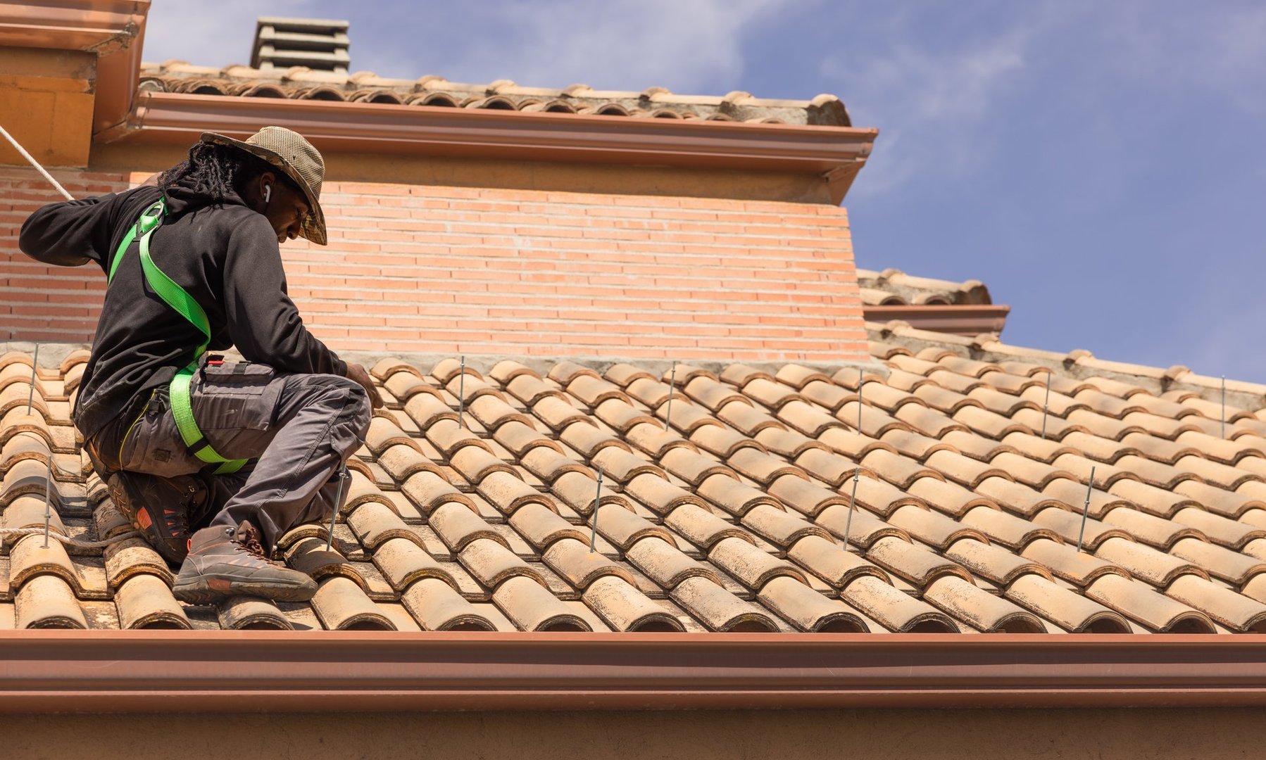 Young man working on a rooftop, installing photovoltaic solar panels, wearing safety harness