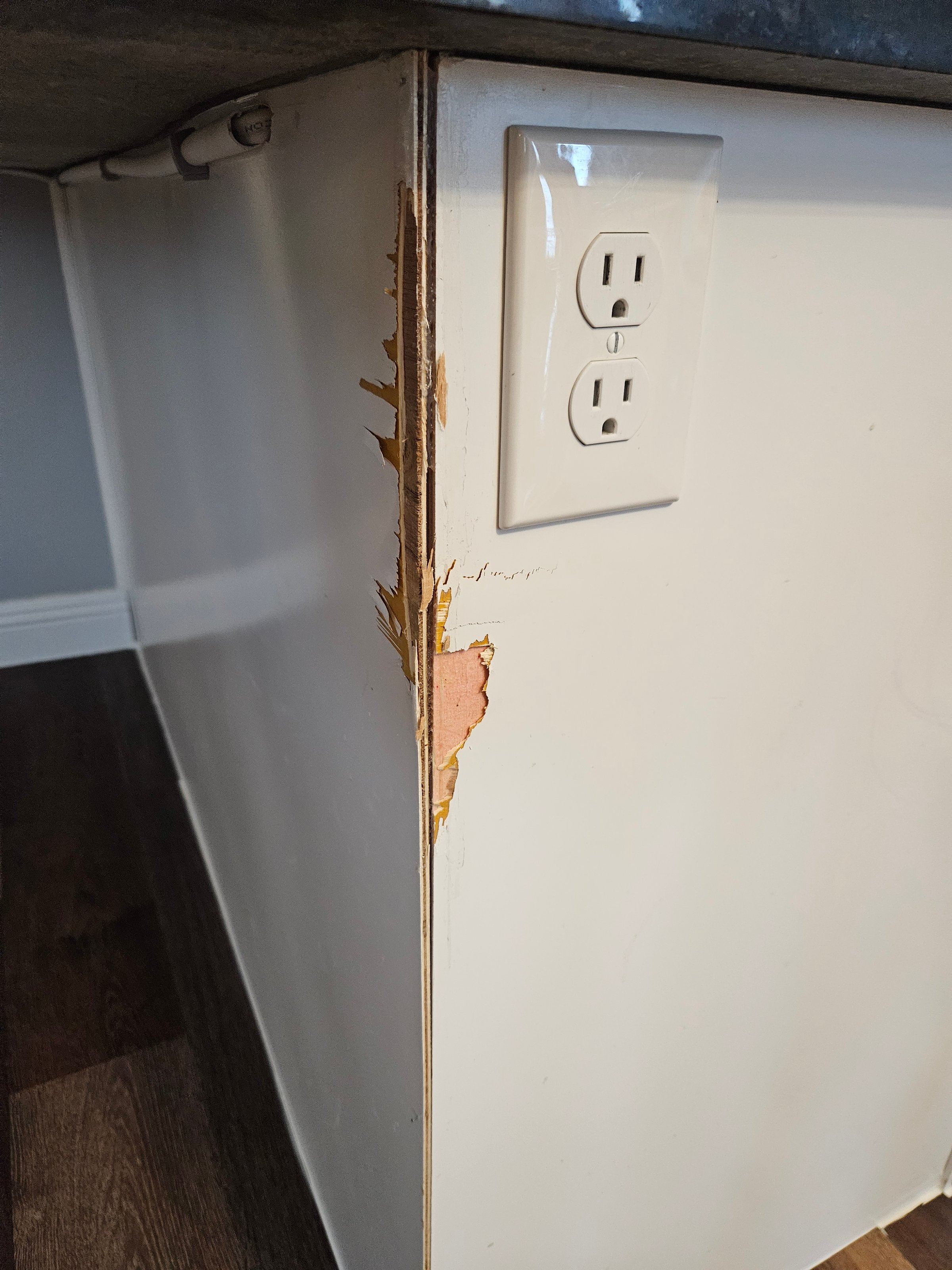 Damaged corner of kitchen peninsula after trim removal showing exposed MDF