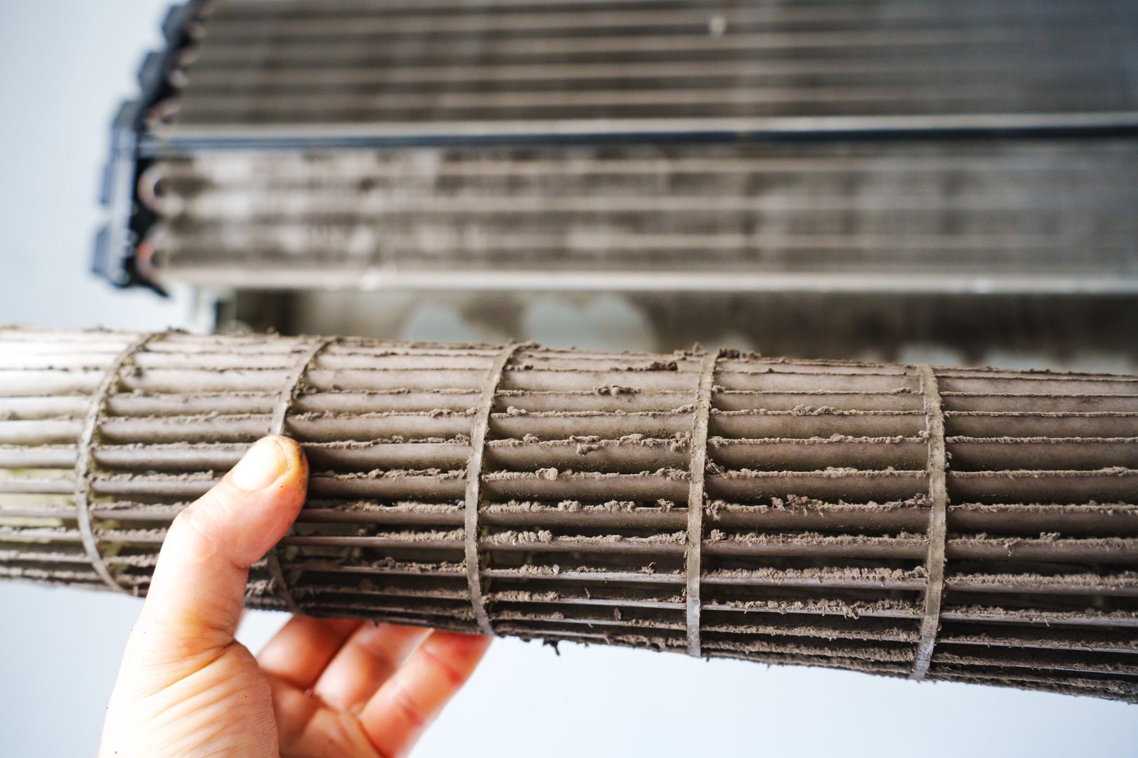 A person holds a dirty air conditioner filter, showing dust buildup. This maintenance activity aims to enhance indoor air quality and ensure efficient cooling performance.