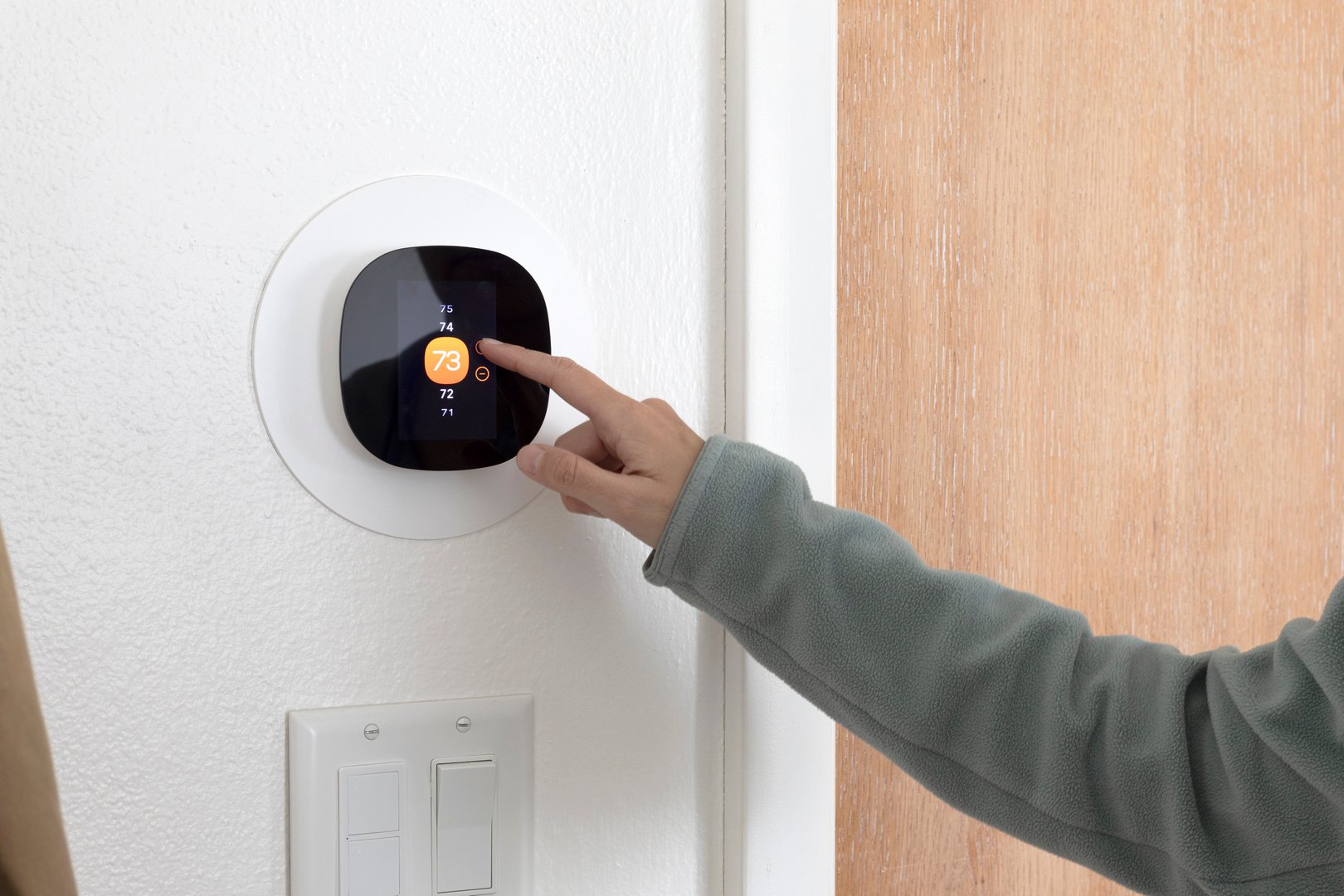 A person using a smart thermostat to increase the room temperature