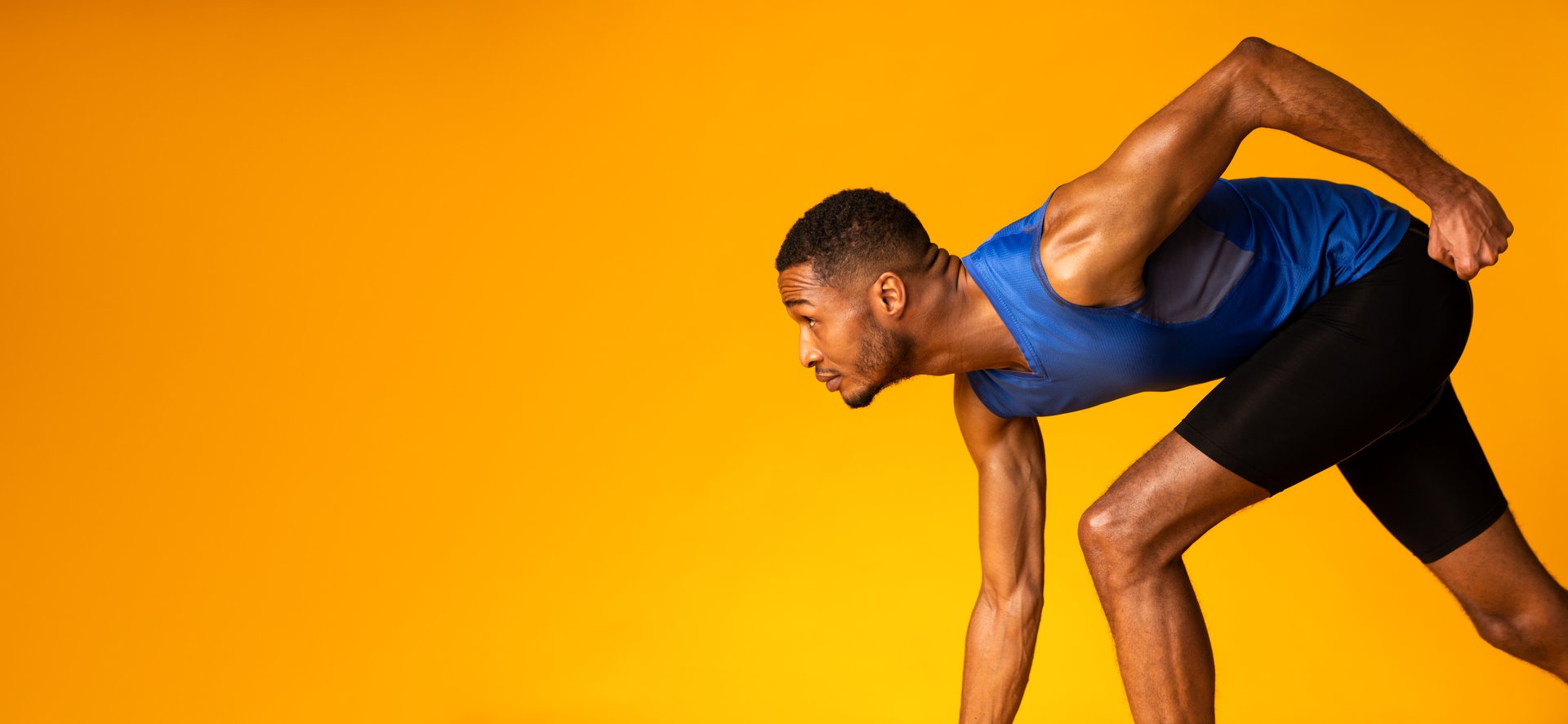Competition. Confident black sportsman preparing for a run, looking up at copyspace, panorama, yellow studio wall