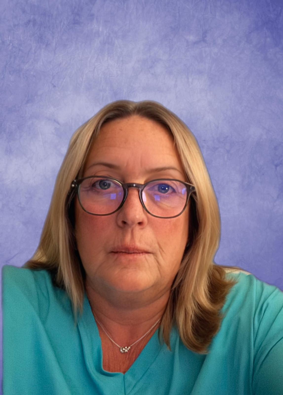 A woman with glasses and shoulder-length blonde hair, wearing a turquoise top, against a textured blue background.