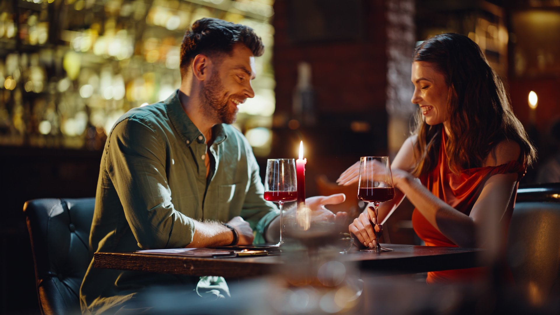 Affectionate man taking woman hand confessing in love at cozy restaurant closeup. Smiling couple having romantic date sitting bar table with wine glasses. Sweet pair enjoying intimate moments together
