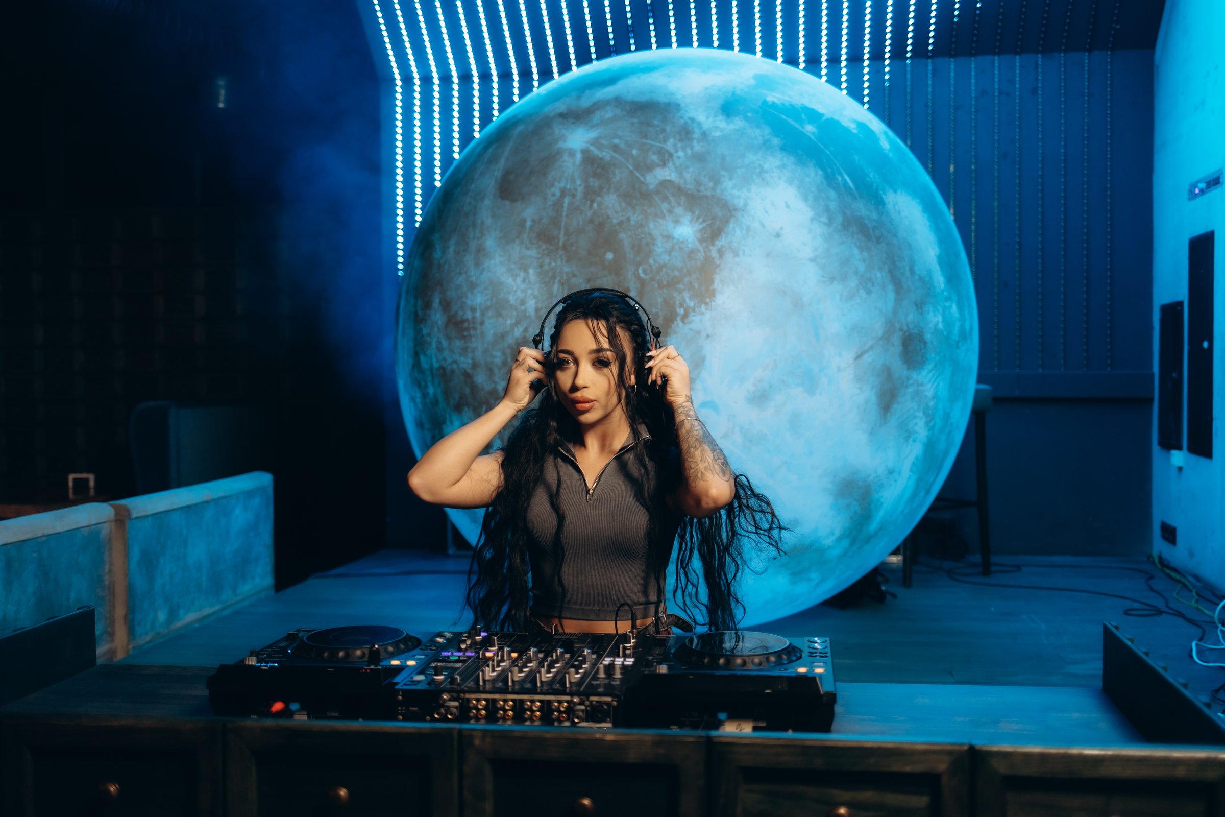 A female DJ in a modern nightclub setting performing music. The illuminated moon backdrop and stylish visuals create an atmosphere of energy, nightlife, and entertainment.