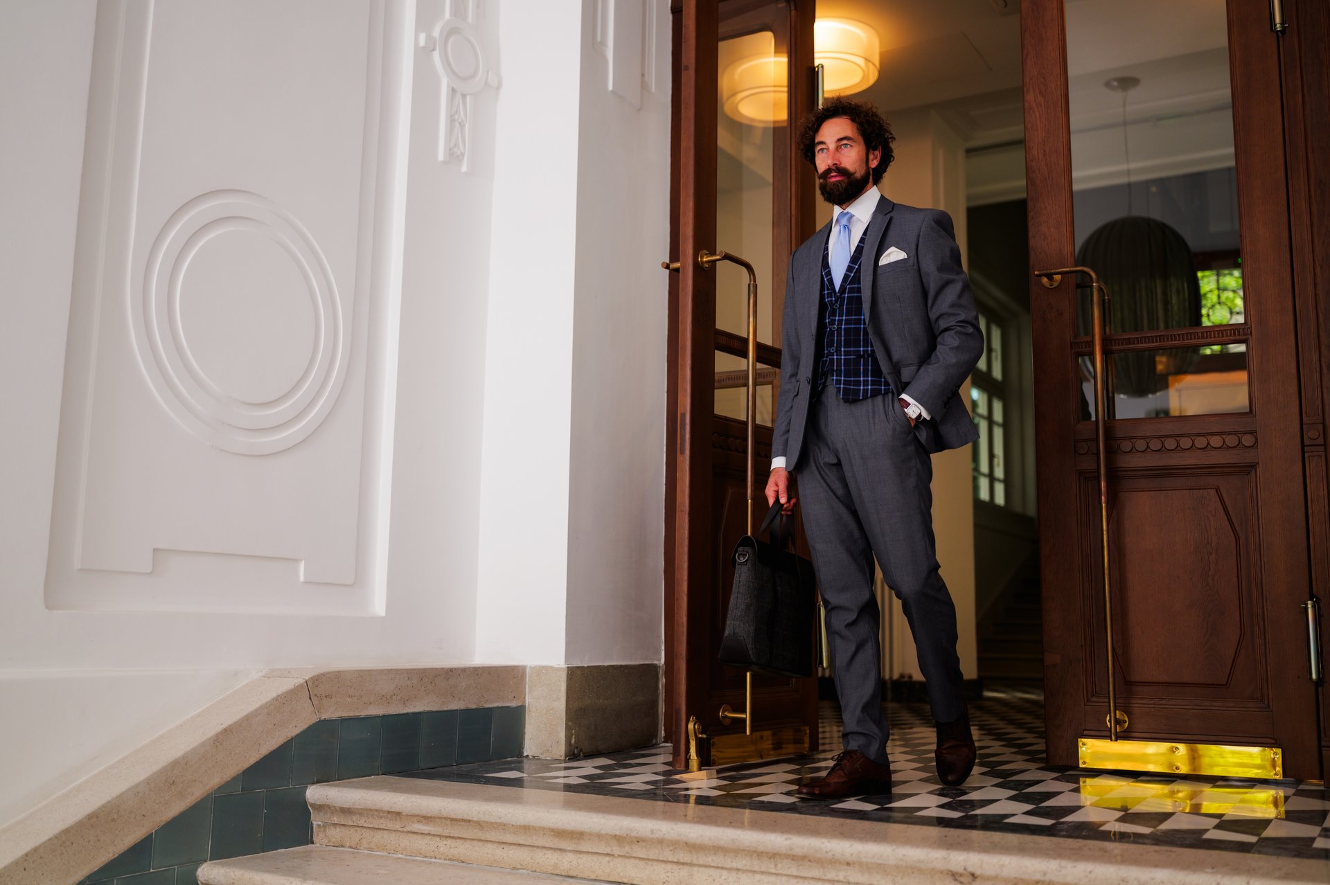 Confident businessman dressed in a stylish suit and carrying a briefcase, exiting a luxurious building, radiating success and professionalism while embodying ambition and elegance