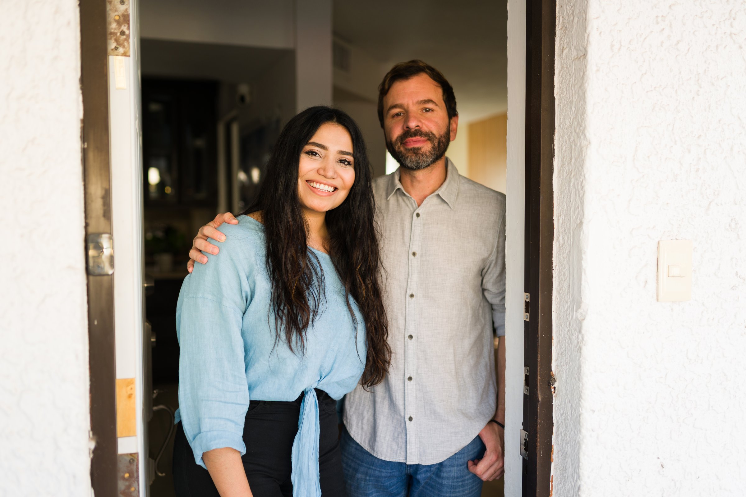 Happy couple standing at their home's open front door, smiling