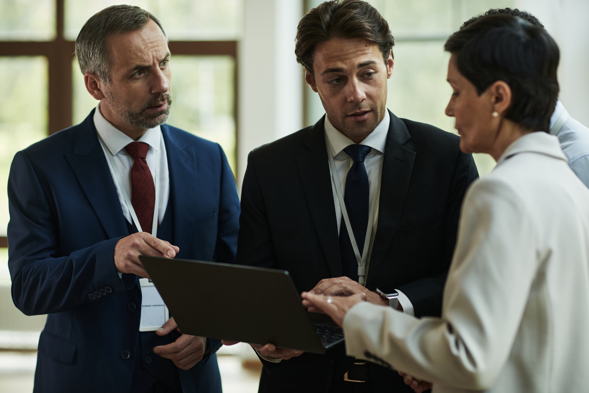 Caucasian middle aged man discussing business strategy with young male colleague and mature woman in suits using laptop during corporate meeting in office setting