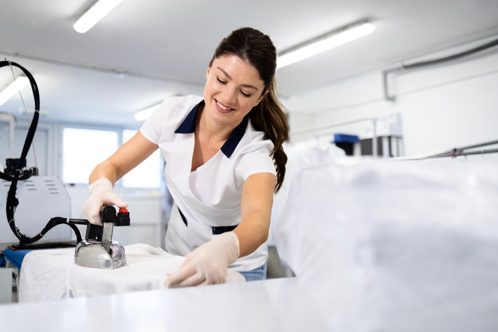 Female worker ironing clothes in dry cleaning service.