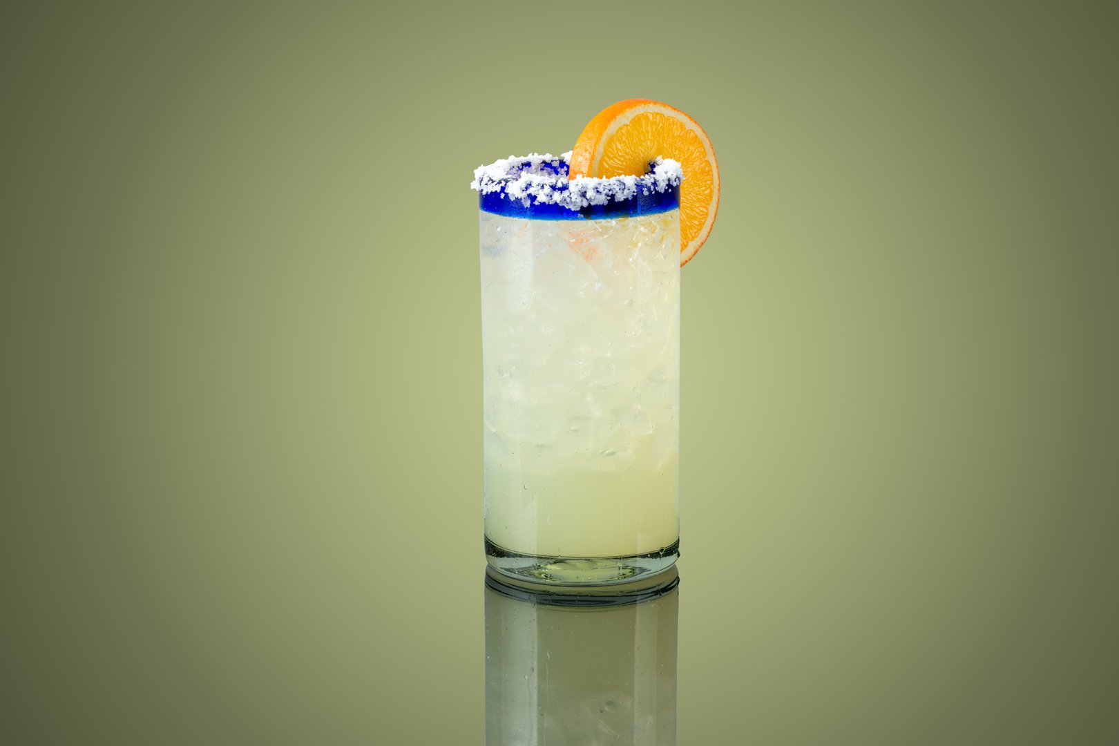 Margarita in a tall glass with a salted rim, a slice of orange on the glass and a dark background.