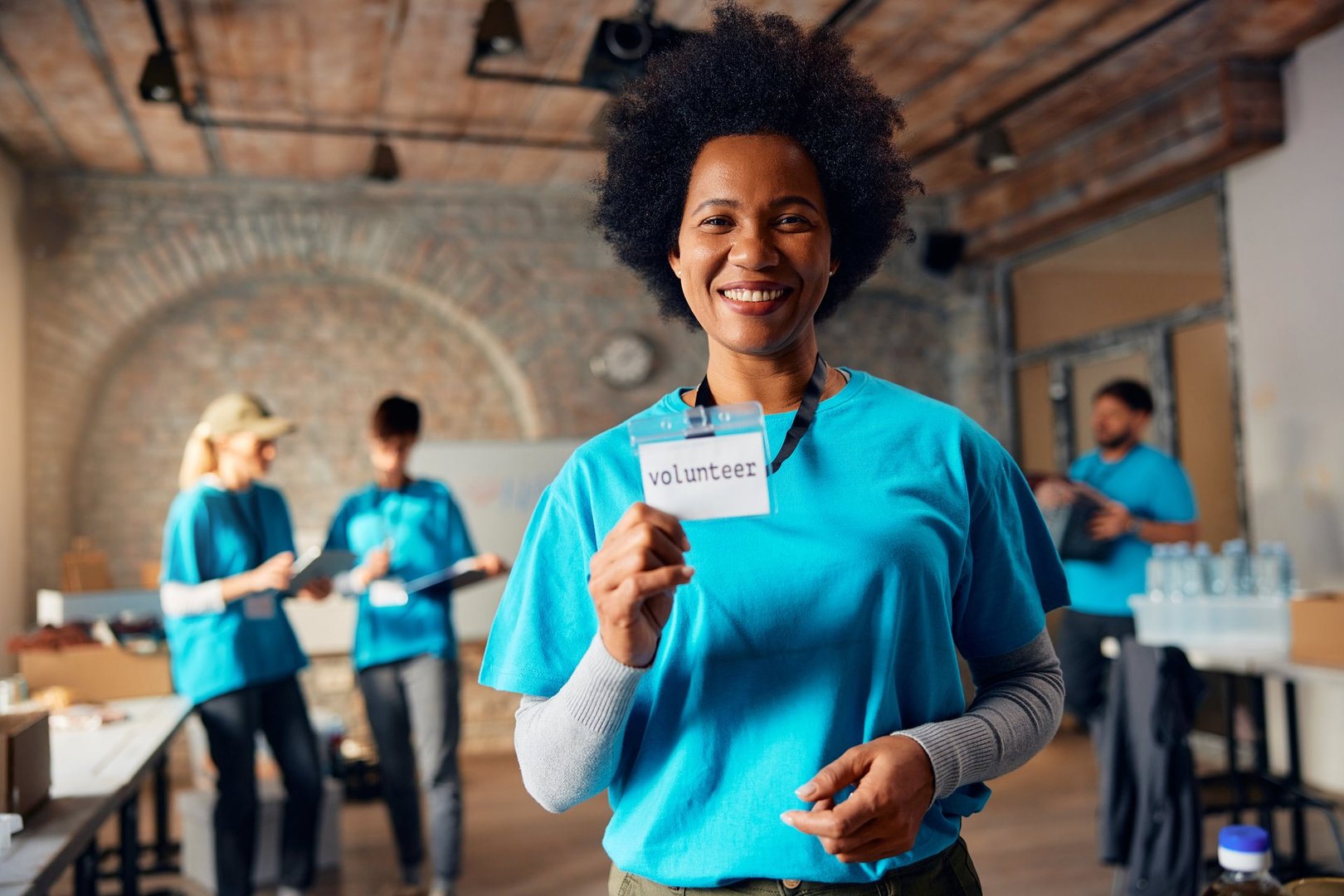 Proud African American volunteer holding her ID card while working at charitable foundation and looking at camera.