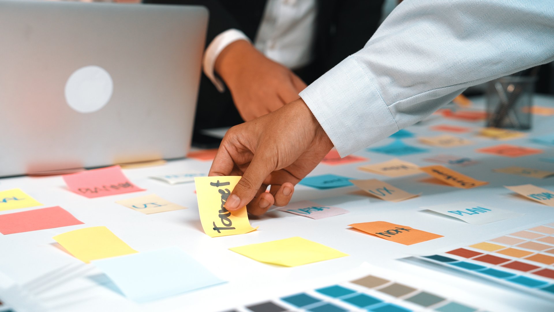 A dynamic office scene showcases hands engaged in a brainstorming session, with colorful sticky notes spread across a table, reflecting creativity and collaboration. SACTR