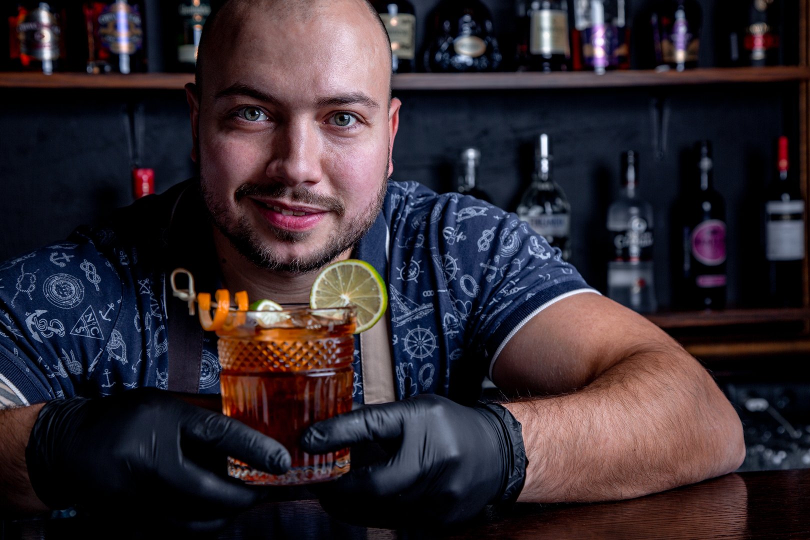 Bartender sirviendo coctel detrás de la barra usando guantes de nitrilo negros.