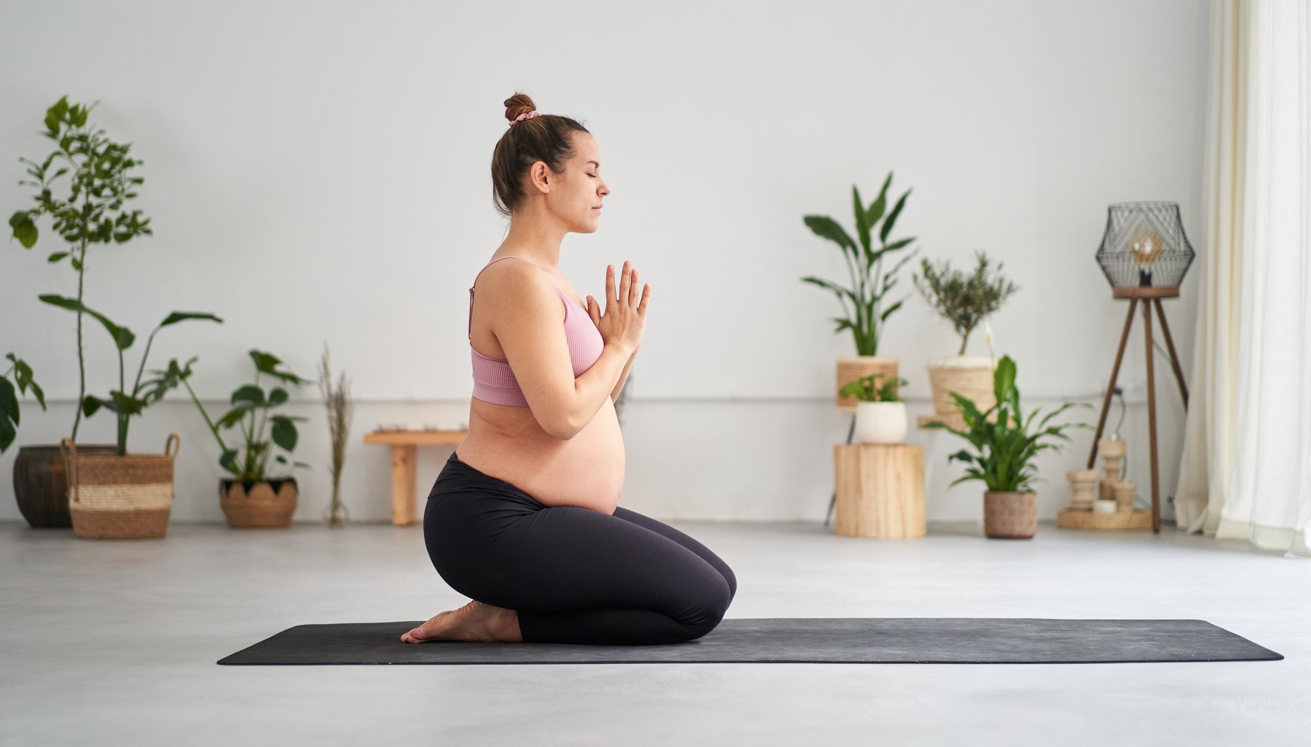 Side view portrait of young pregnant Caucasian woman doing yoga exercises and meditating in class. Female fitness and future motherhood. Concept of health care, mindfulness, relaxation and wellness.