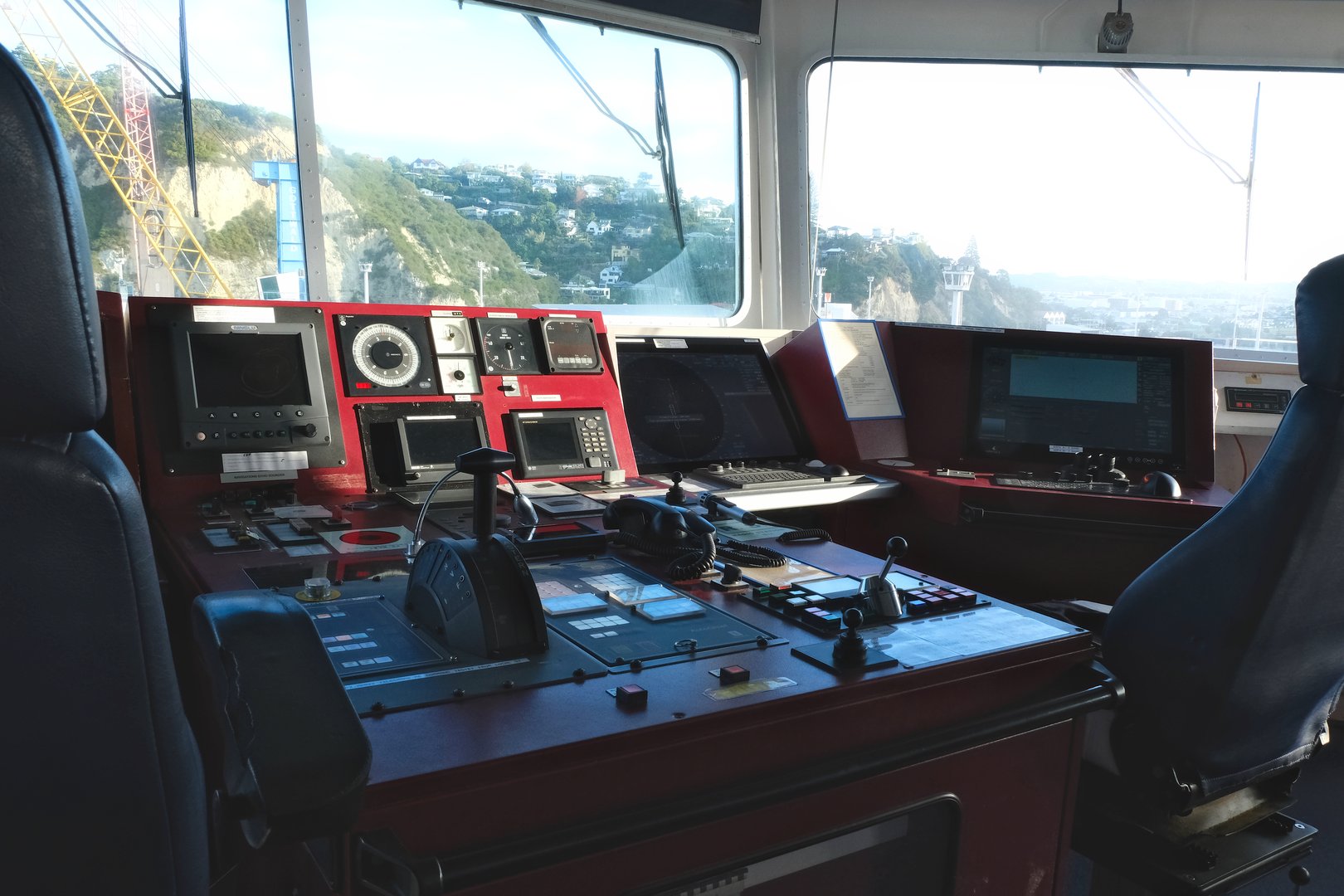 Napier, New Zealand 04 26 2025: Modern Ship's Bridge control console with navigational equipment and chairs of container ship with view on Napier port.
