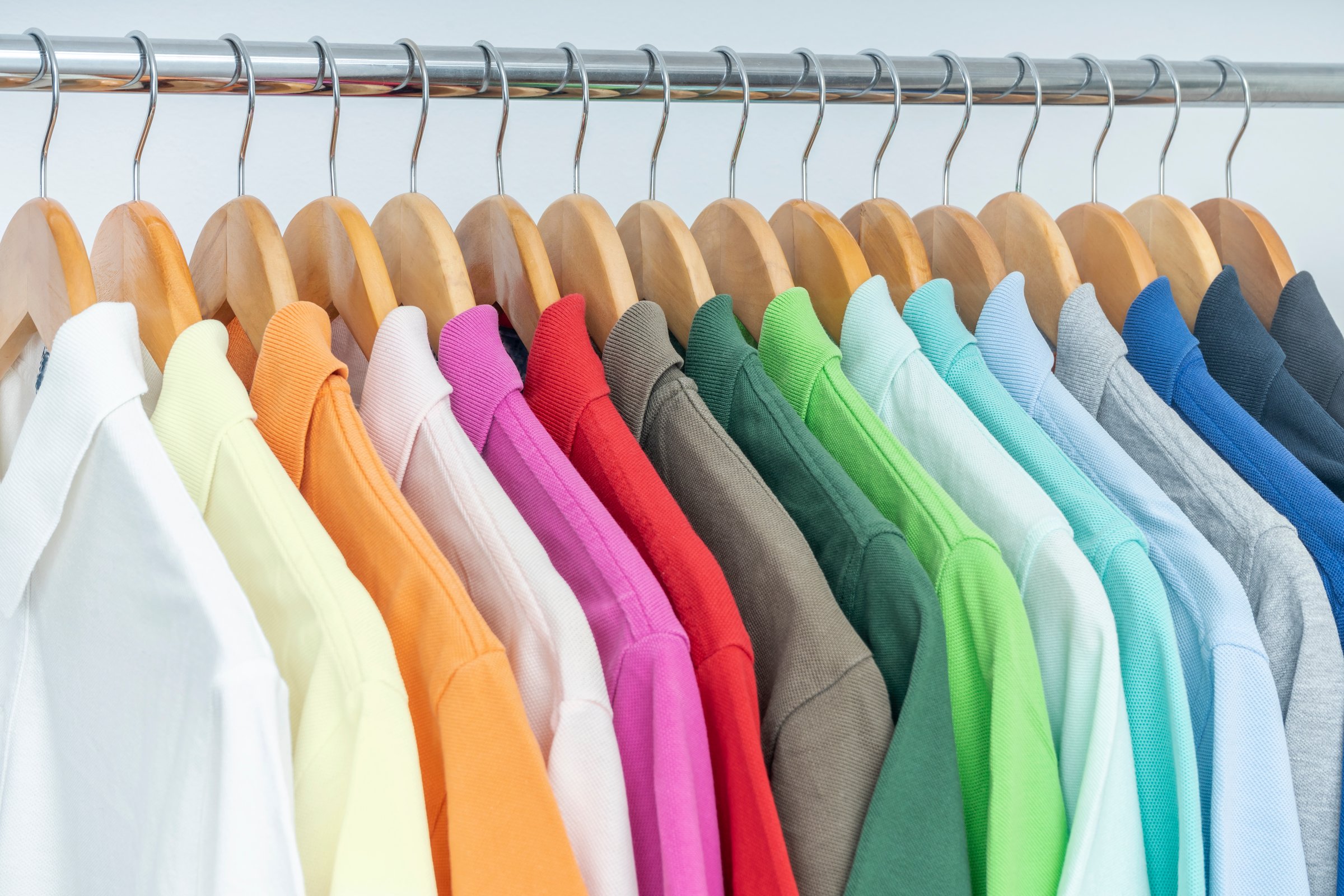 ORGANIZED COLORFUL POLO SHIRTS HANGING ON THE RACK, CLOSET, WARDROBE, DRESSING ROOM OR STORE. SALES AND SHOPPING CONCEPT. SUMMER MENSWEAR COLLECTION.
