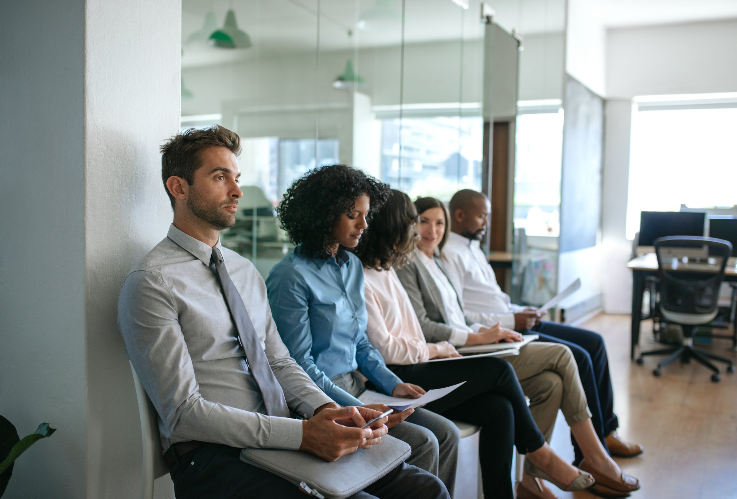 Diverse group of job applicants sitting together outside of an office waiting to be interviewed