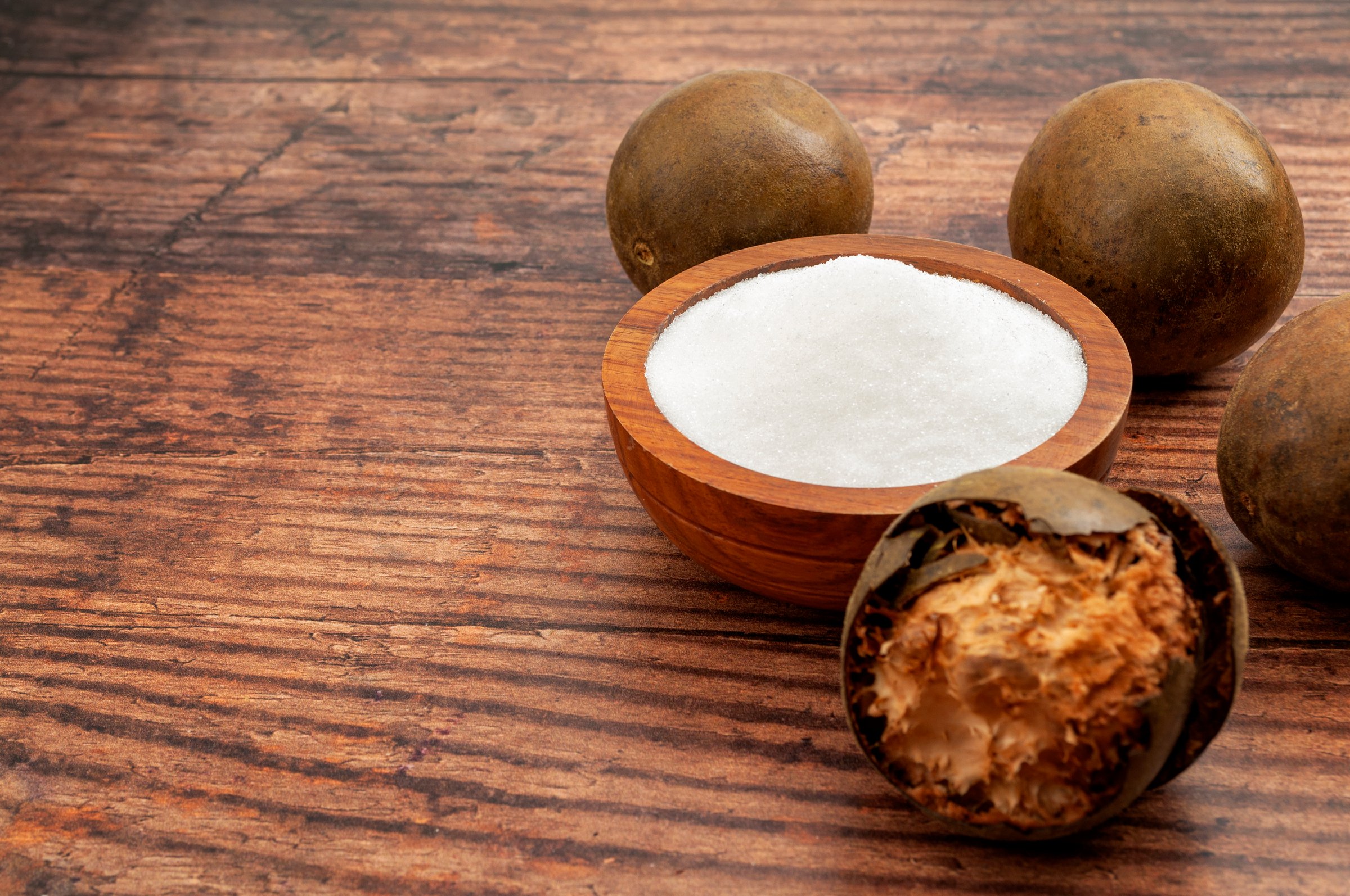 Low calorie alternative to sugar and natural remedy to inflammatory disease and arthritis concept with Luo Han Guo or monk fruit and bowl of sweetener isolated on wood background with copy space