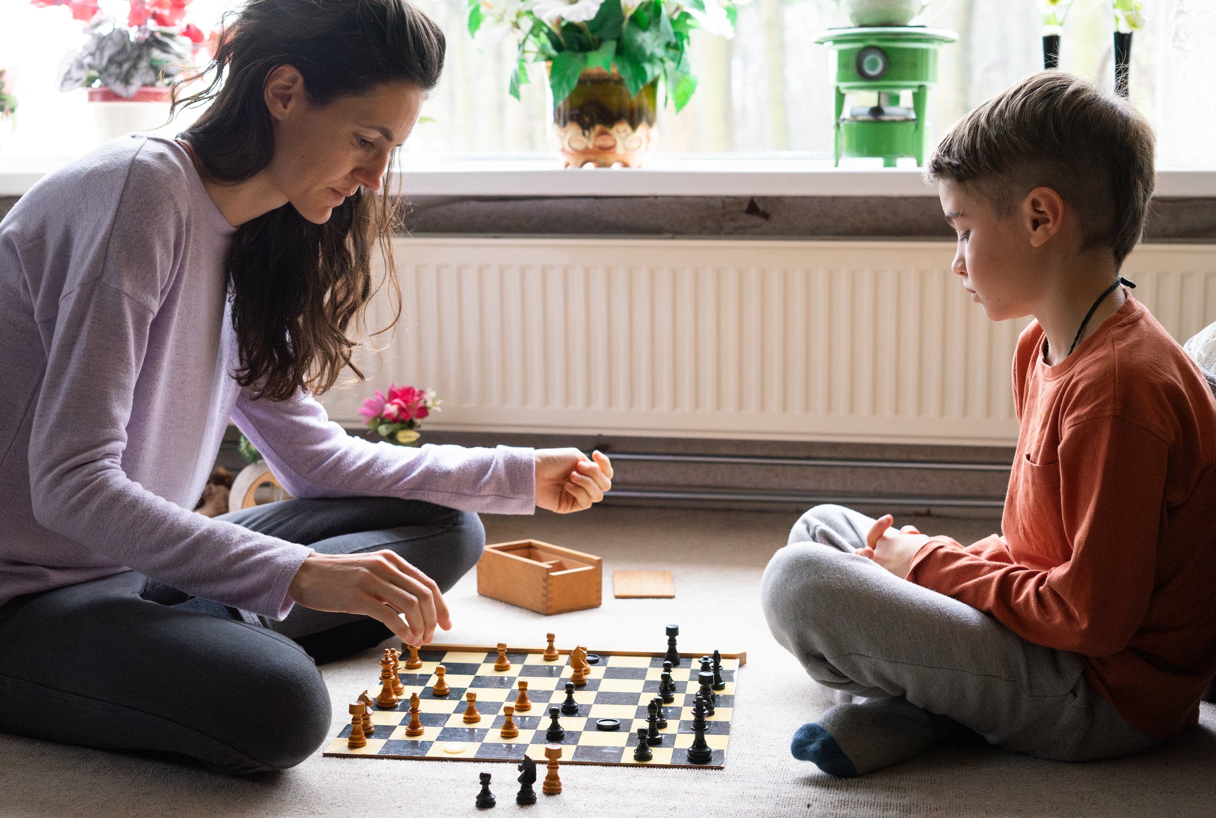 Mother and son concentrating while playing chess on the floor in the living room