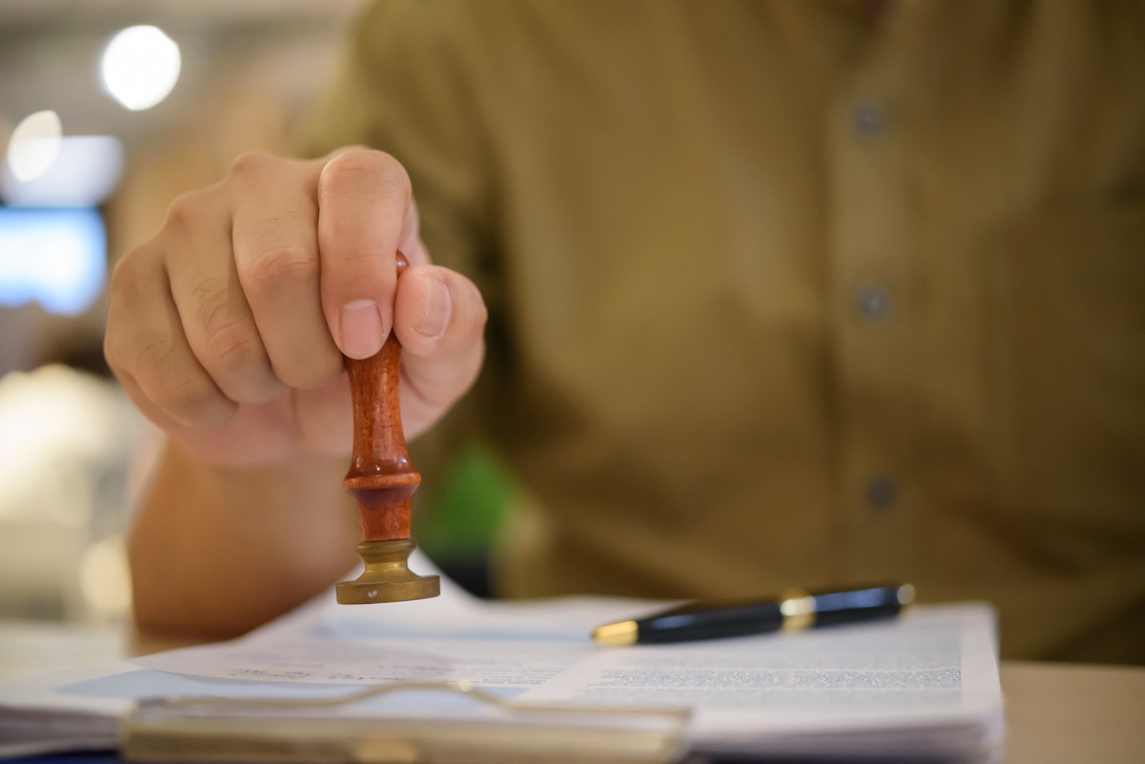 Hand using a rubber stamp on official papers, representing approval process, legal documentation, and certified paperwork. contract certification, notarization, and business authorization.
