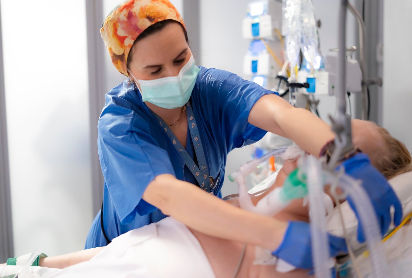 Nurse wearing surgical mask and gloves adjusting ventilator of intubated patient in icu