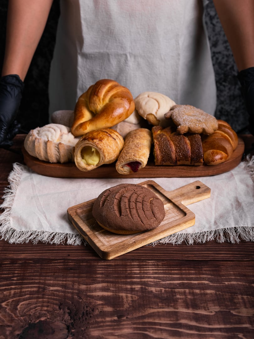 Chocolate concha bread on a rustic wooden table. Background with a variety of typical Mexican sweet breads.