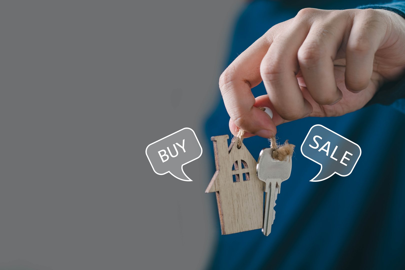 Hand holding house key with wooden keychain, symbolizing real estate transaction and the concepts of buying and selling.