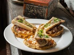 Plate with sopes topped with bone marrow and garnished with herbs, on a rustic wooden table.