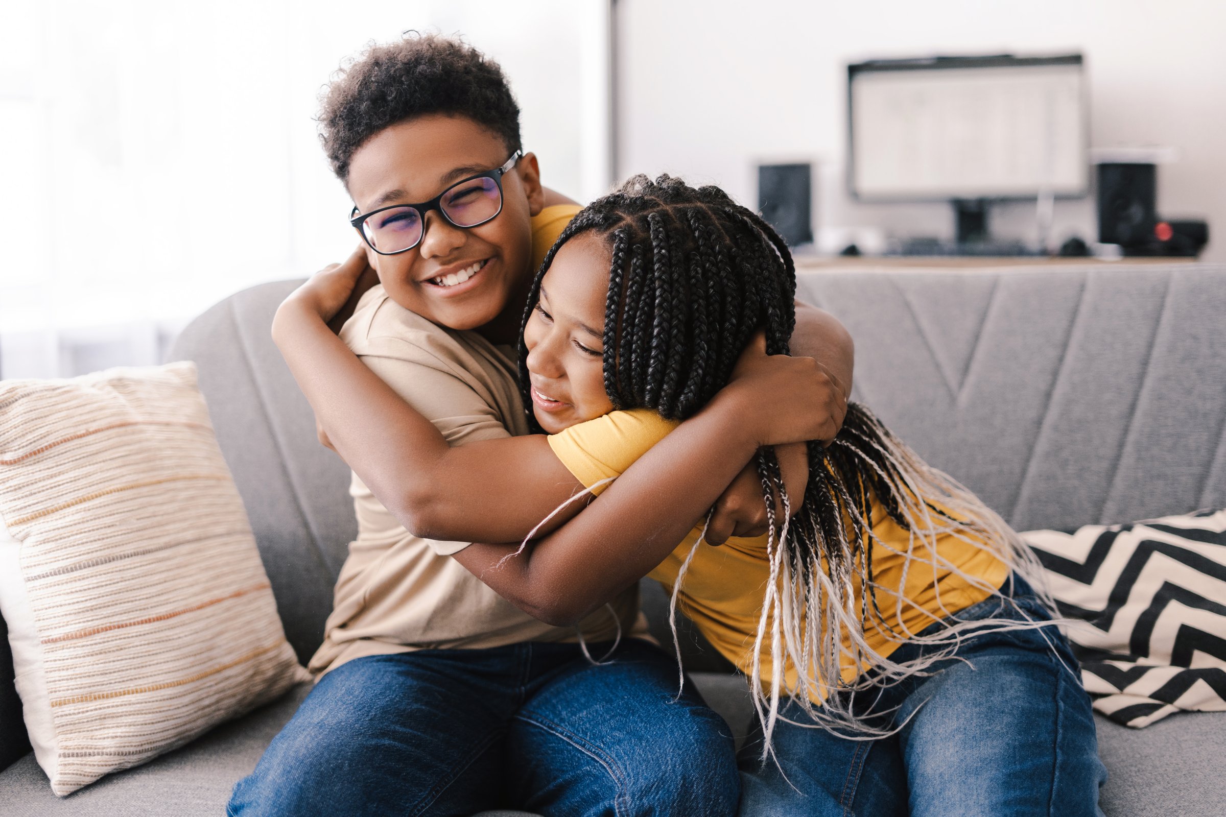 Brother and sister hugging on sofa at home, cozy family moment