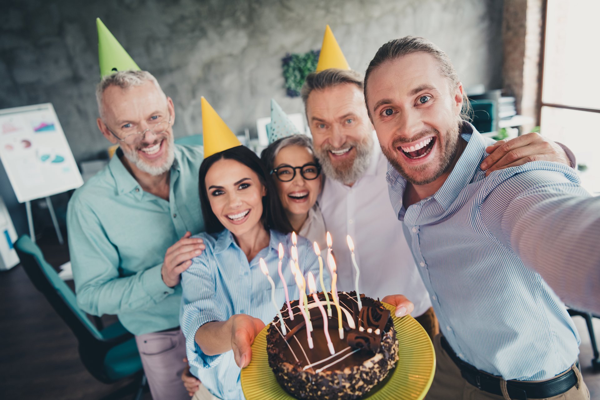 Photo of five successful corporate colleagues embrace hold birthday cake make selfie loft interior office indoors.