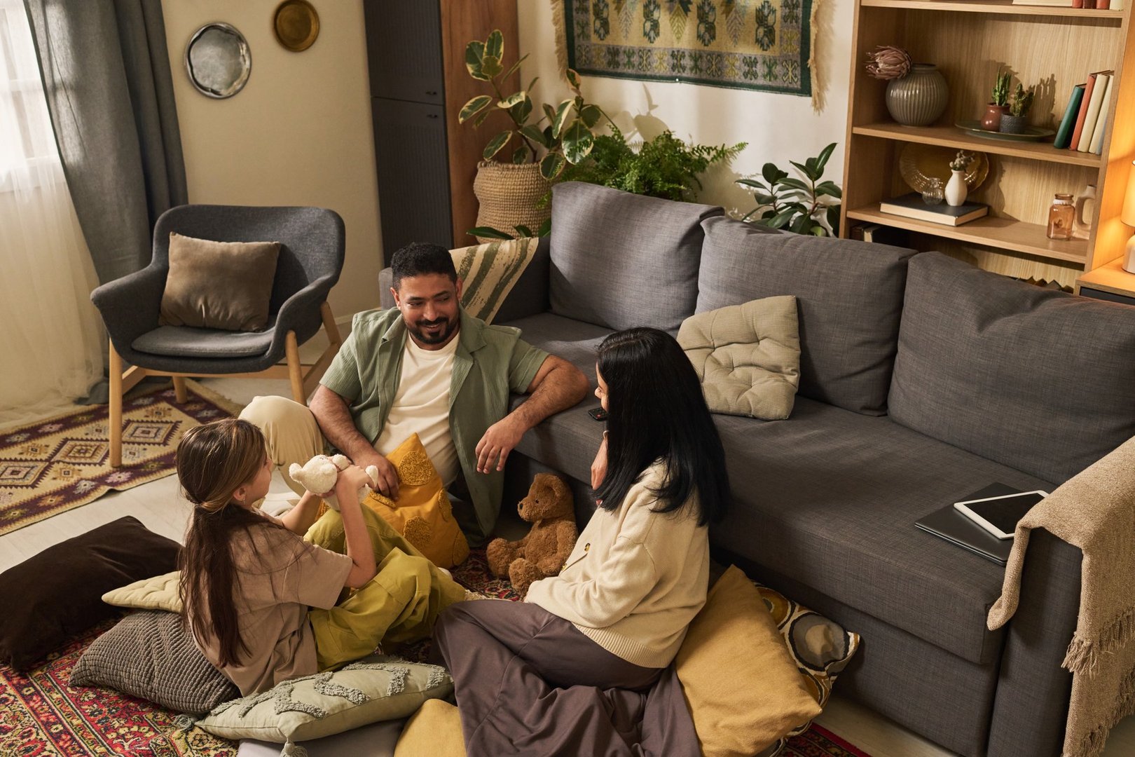 Family enjoying quality time together in cozy living room with carpeted floor and modern furniture, playing with plush toys and using electronic device, having fun and bonding