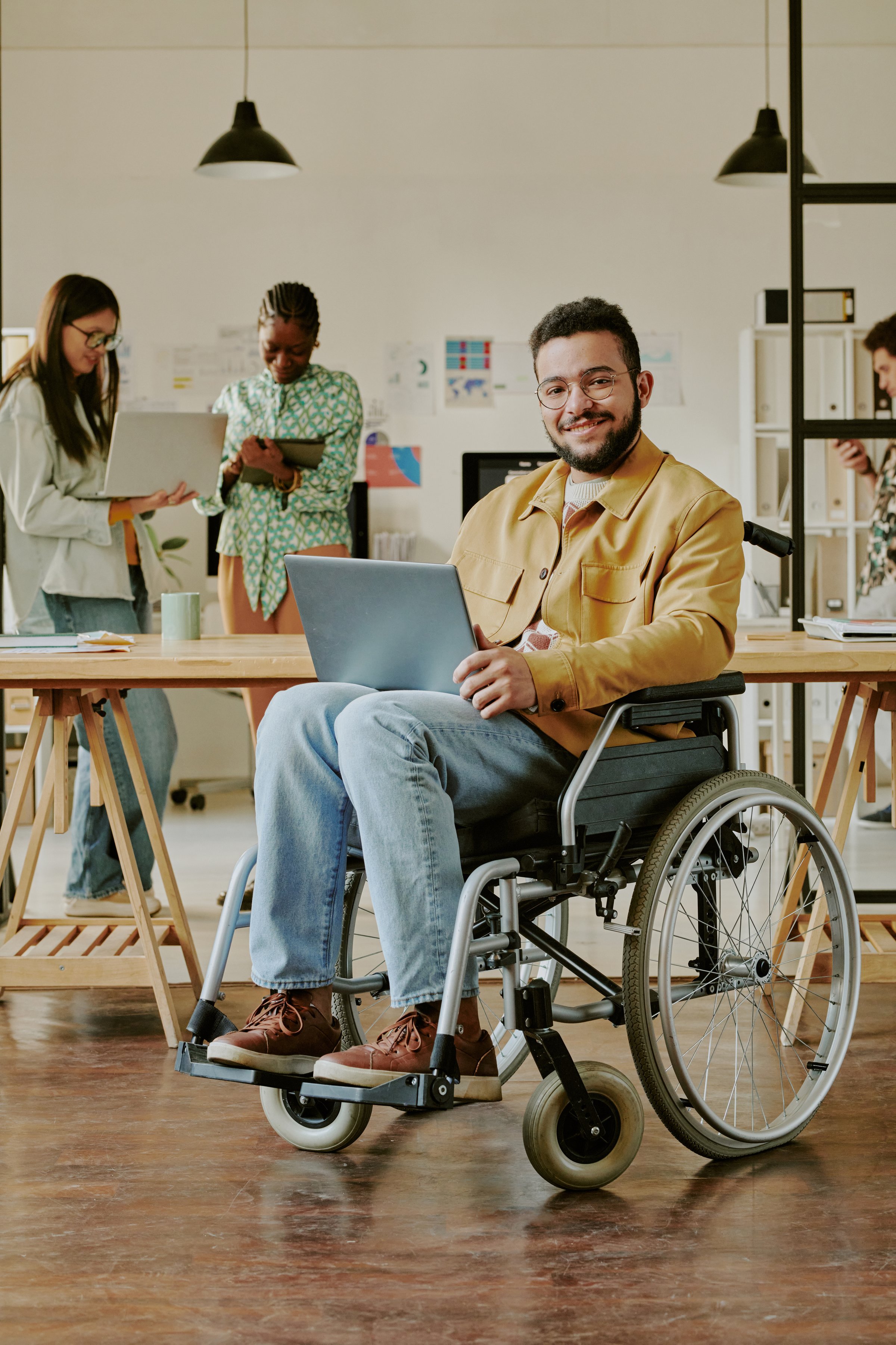 Vertical portrait of highly skilled programmer with disability smiling at camera for portrait in modern office