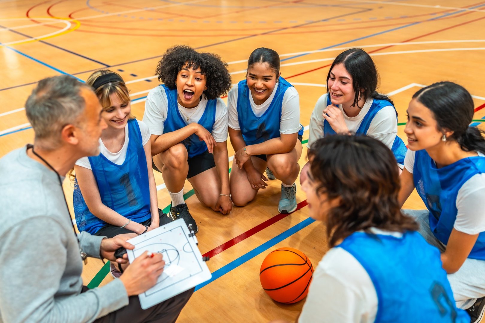 Basketball coach kneeling on the court and explaining game strategy to his female team during a time out