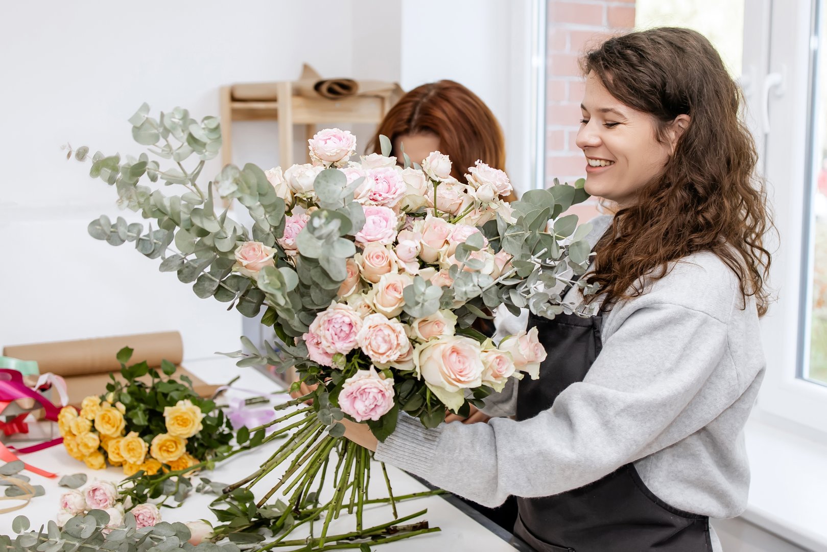Two Female Florists Smiling While Creating a Beautiful Bouquet in a Cozy Workshop Near the Window – Floral Design and Small Business Concept