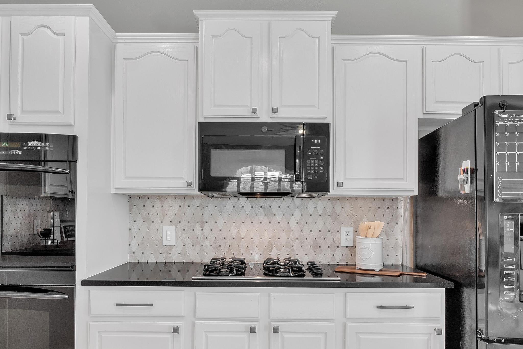 Modern kitchen with white cabinets, black appliances, a black countertop, and a geometric backsplash design.