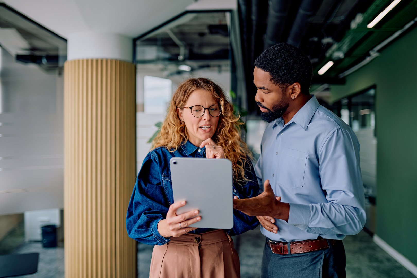 Two diverse business colleagues collaborating, discussing data on a tablet, and working together in a contemporary office setting