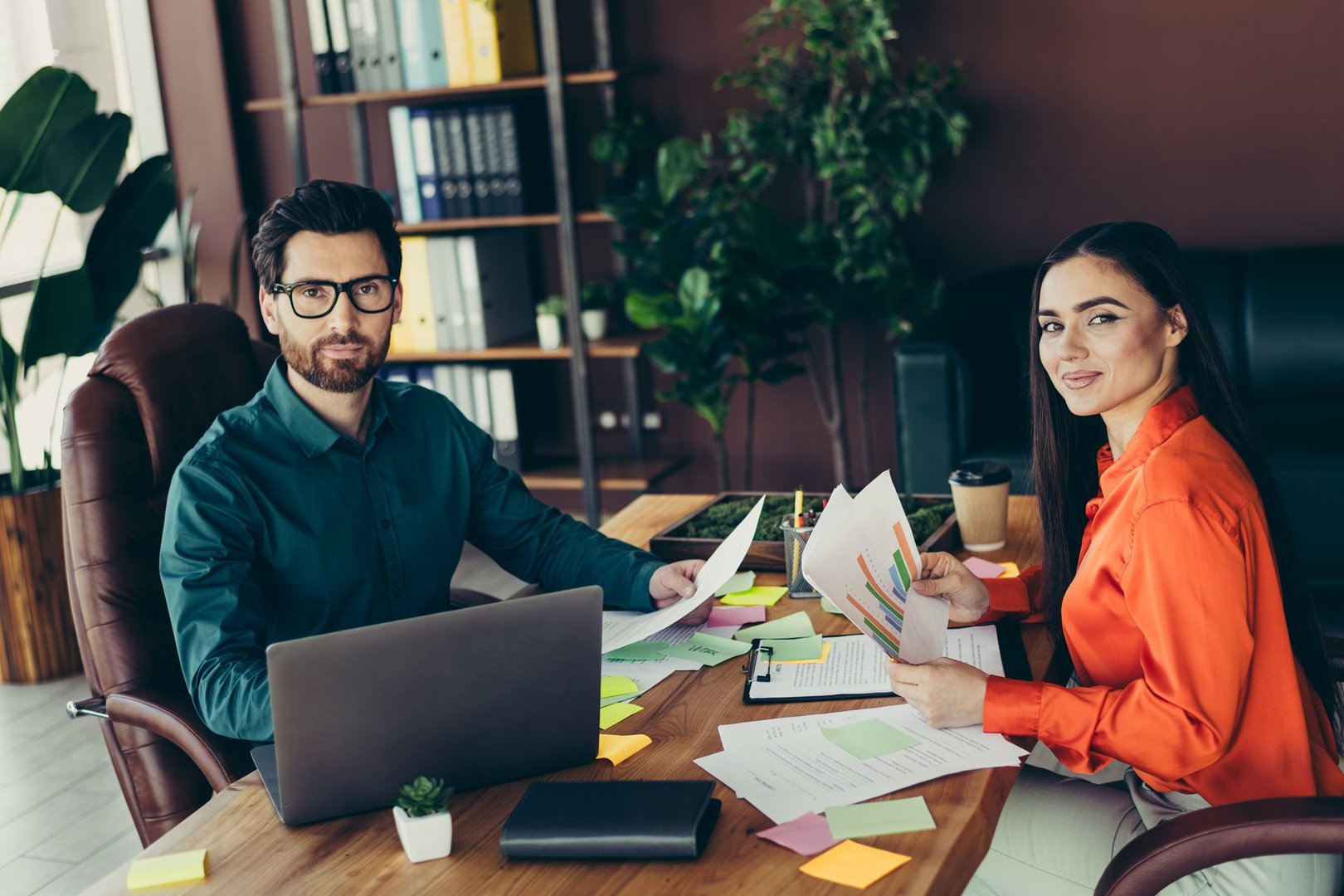 Two colleagues collaborating in a modern office, both reviewing colorful charts, documents, and discussing ideas, fostering professional interaction and productivity.