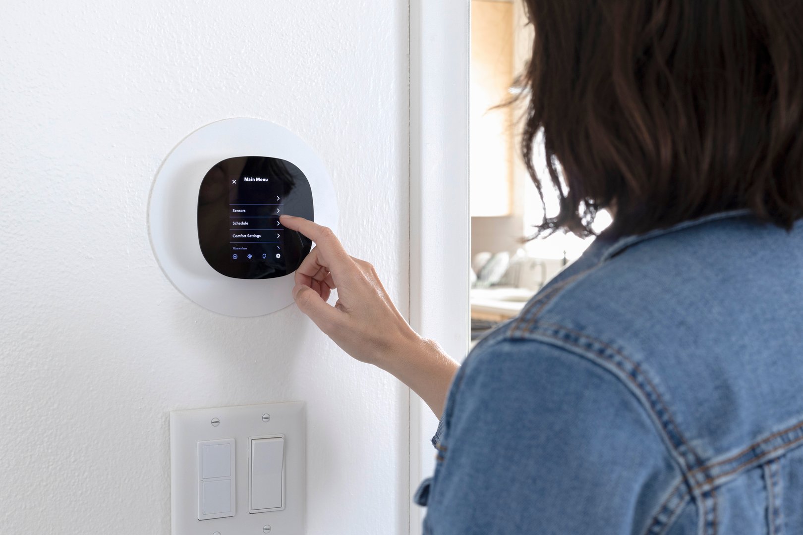 A woman programming a smart thermostat at home