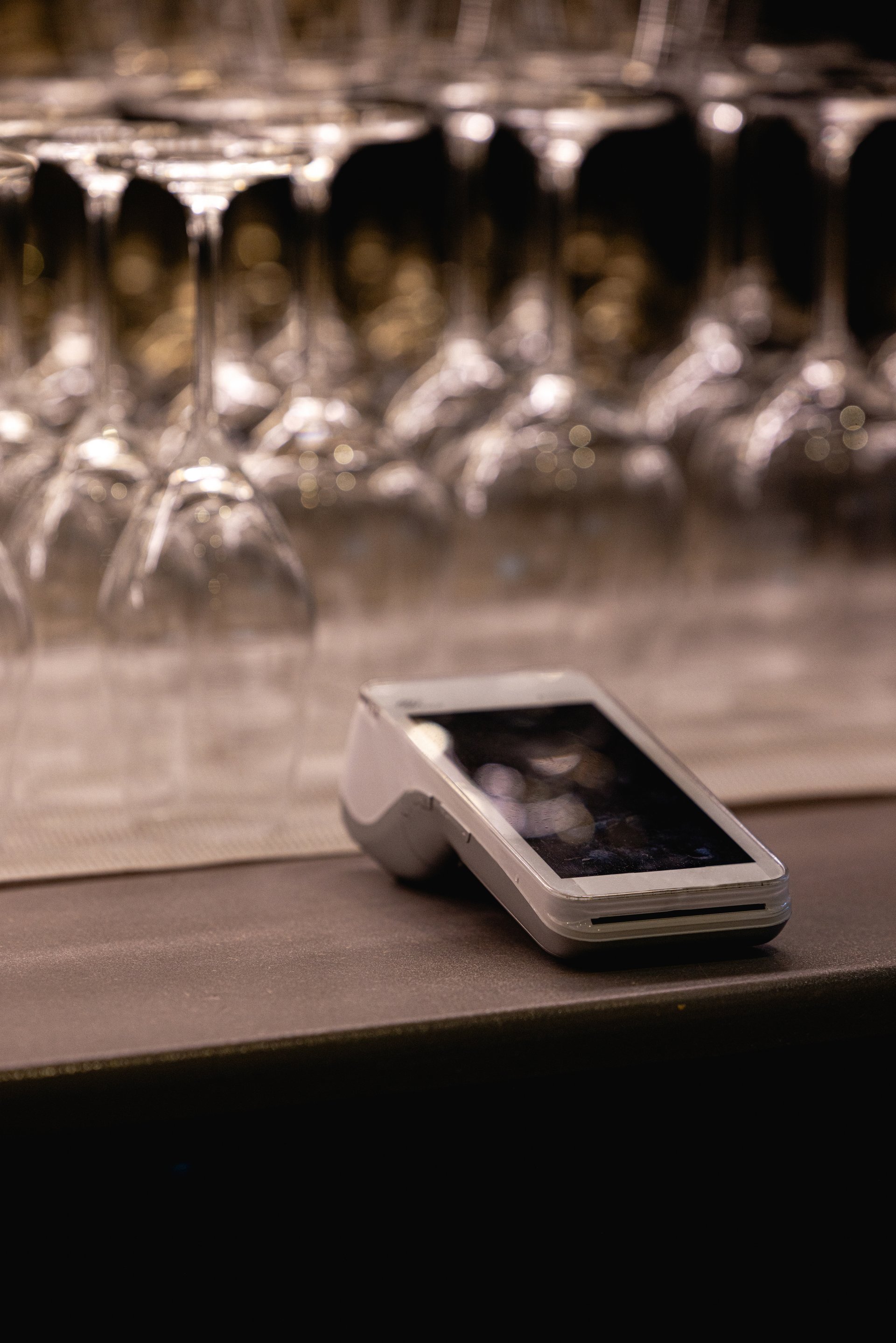 contactless payment terminal or POS terminal against a backdrop of inverted glasses in a restaurant or bar.