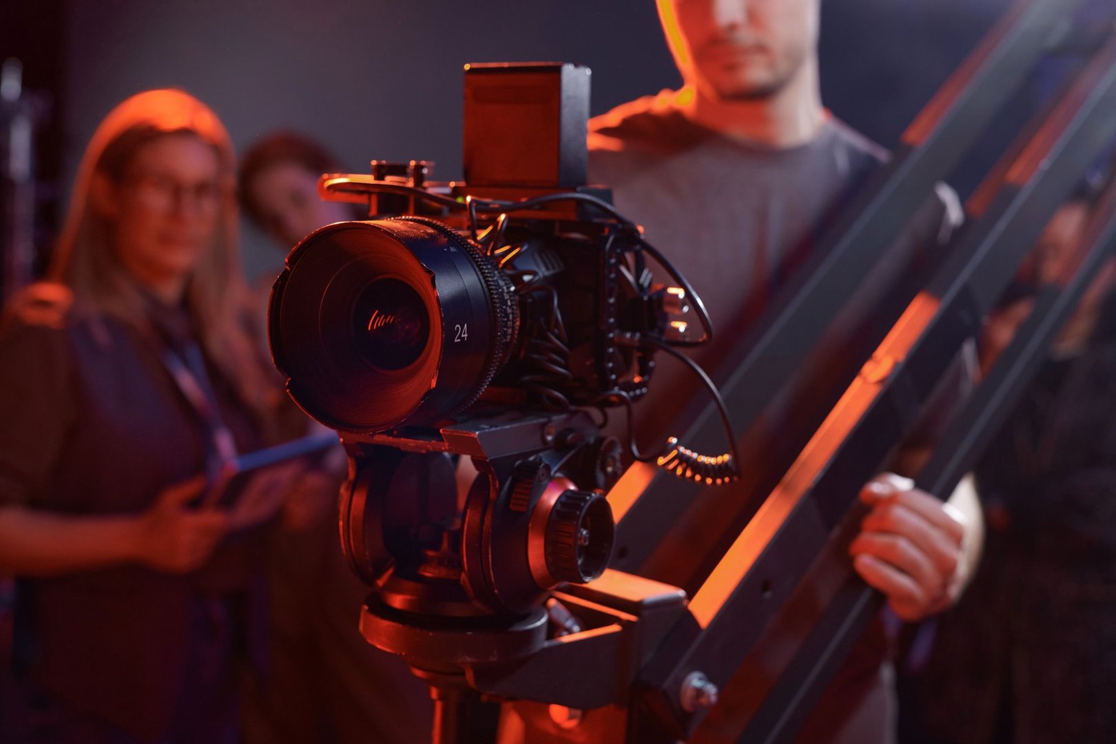 Closeup of cameraman operating video camera on rig in studio with red neon lights copy space