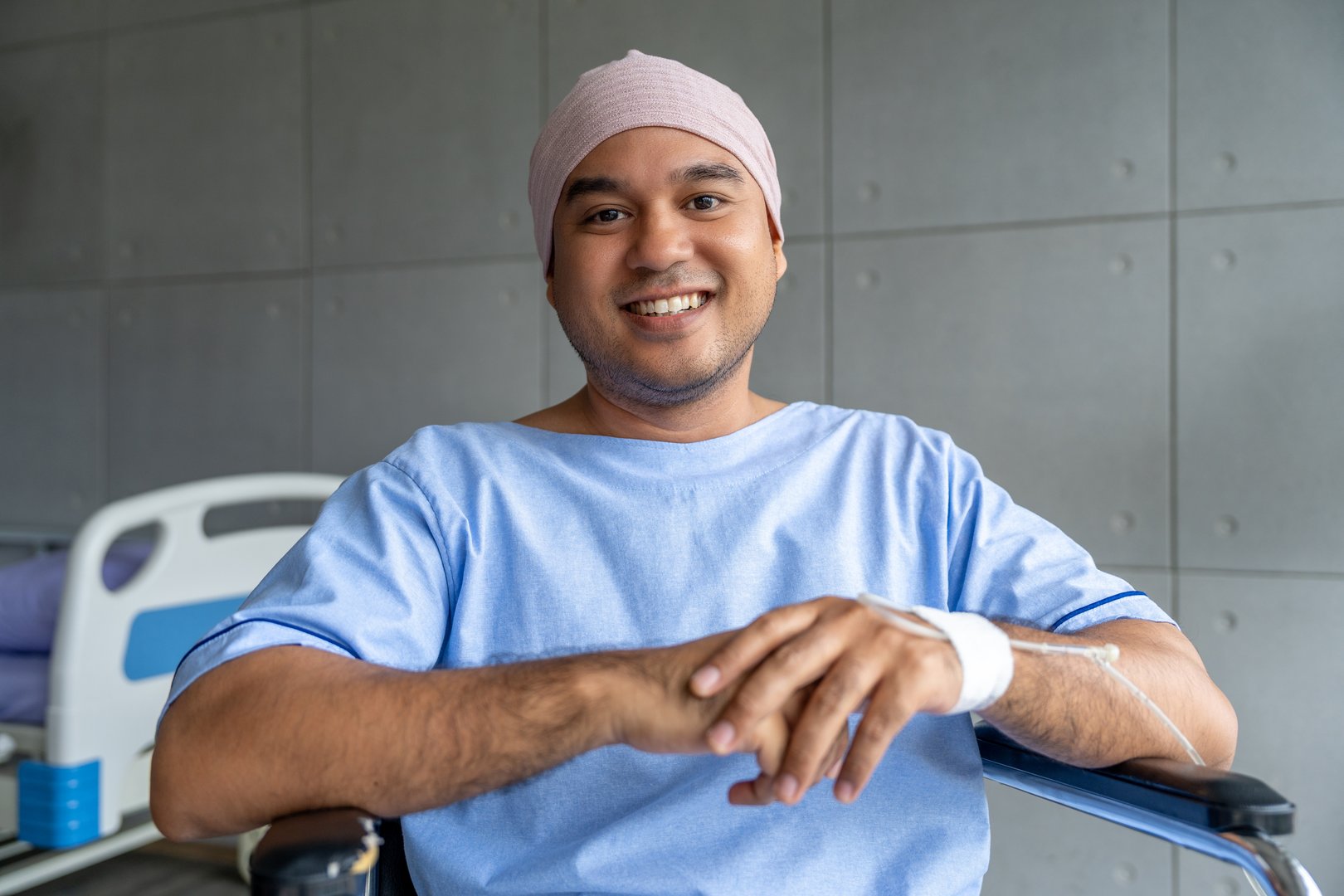 A male cancer patient in a wheelchair with an IV smiles with joy and hope showing strength and positivity during treatment. Man receiving IV therapy in a wheelchair appears happy and uplifted