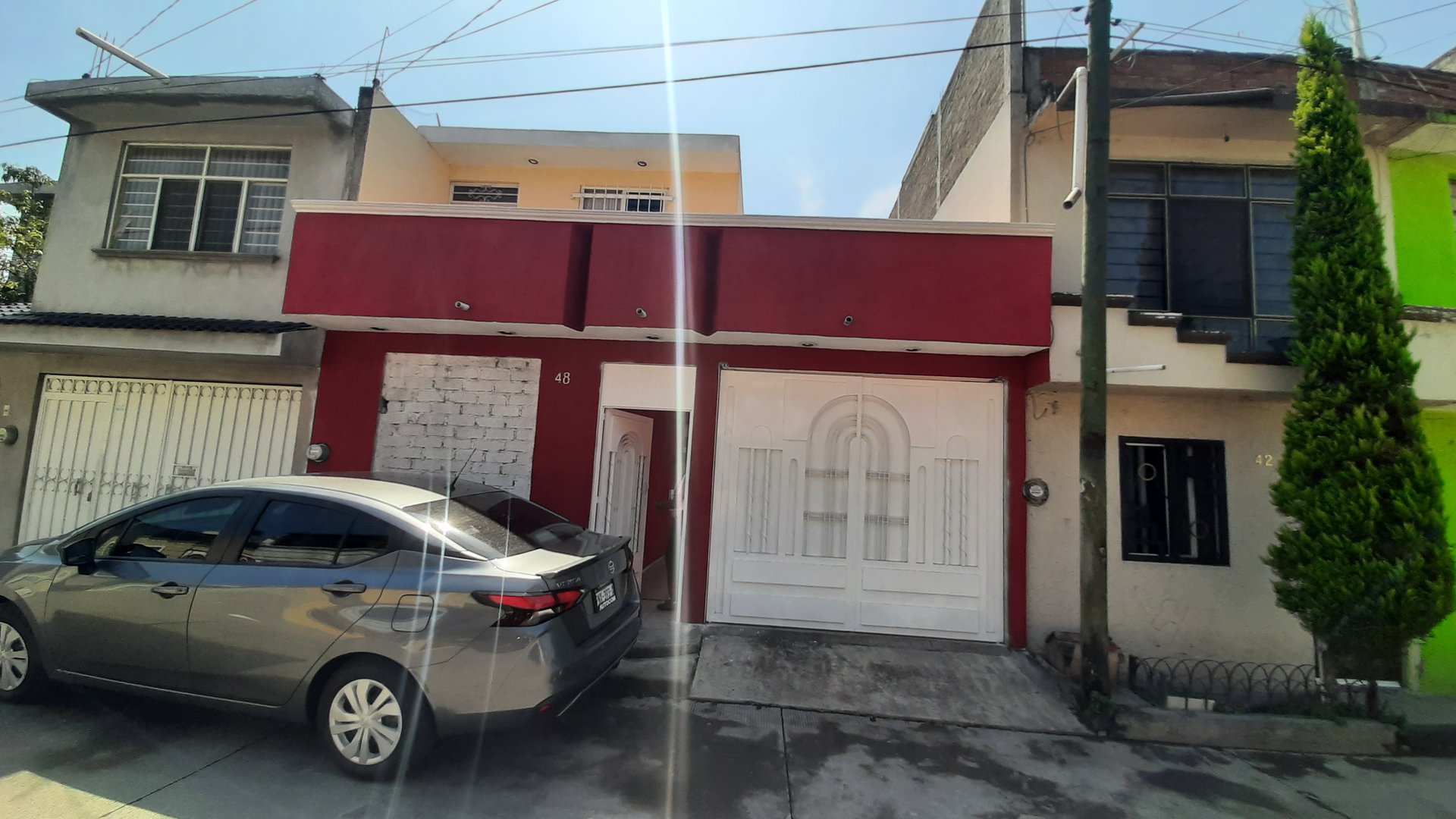 Street view of row houses, one with a red facade and white garage door, a parked gray car in front.