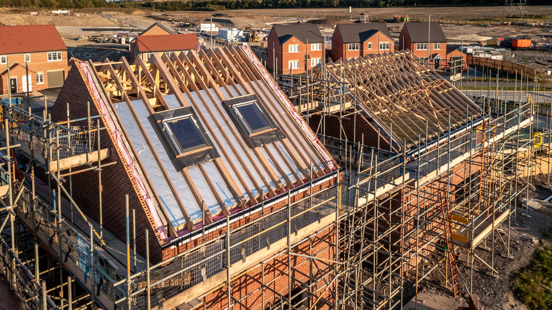Aerial view of a roof under construction with beams and apex supporting exterior skylight windows on a new build house surrounded by scaffolding on a construction site