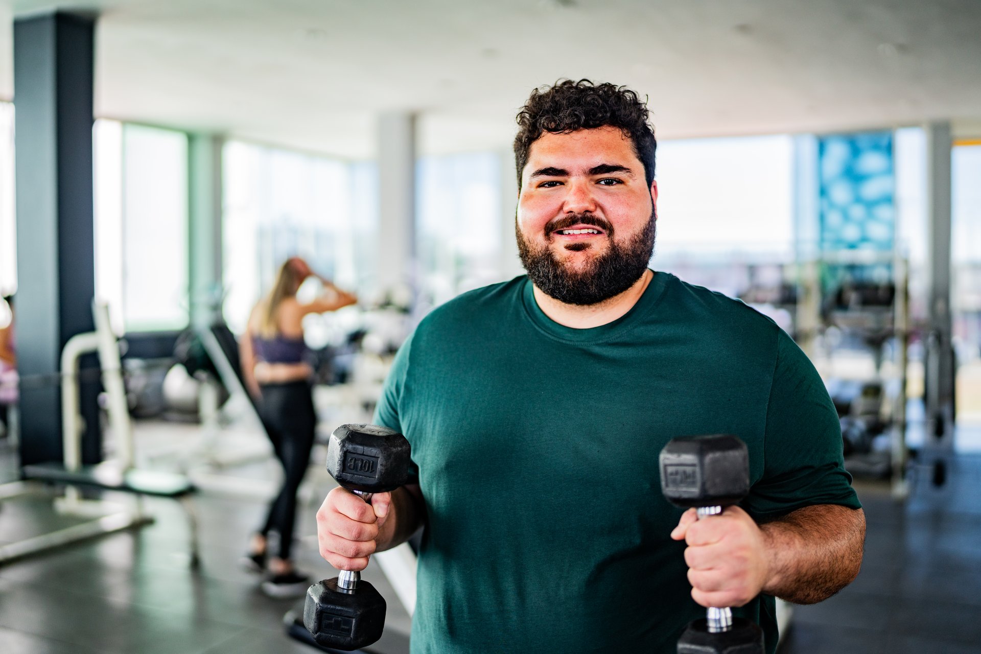 Portrait of mid adult man doing biceps exercises using dumbbell at gym