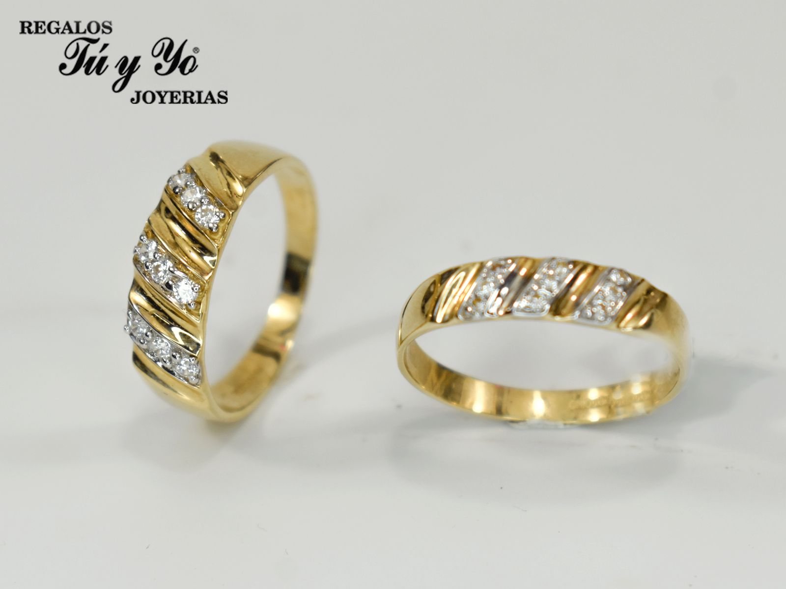 Two gold rings with diagonal diamond accents, one standing upright and the other lying flat, displayed on a white surface.