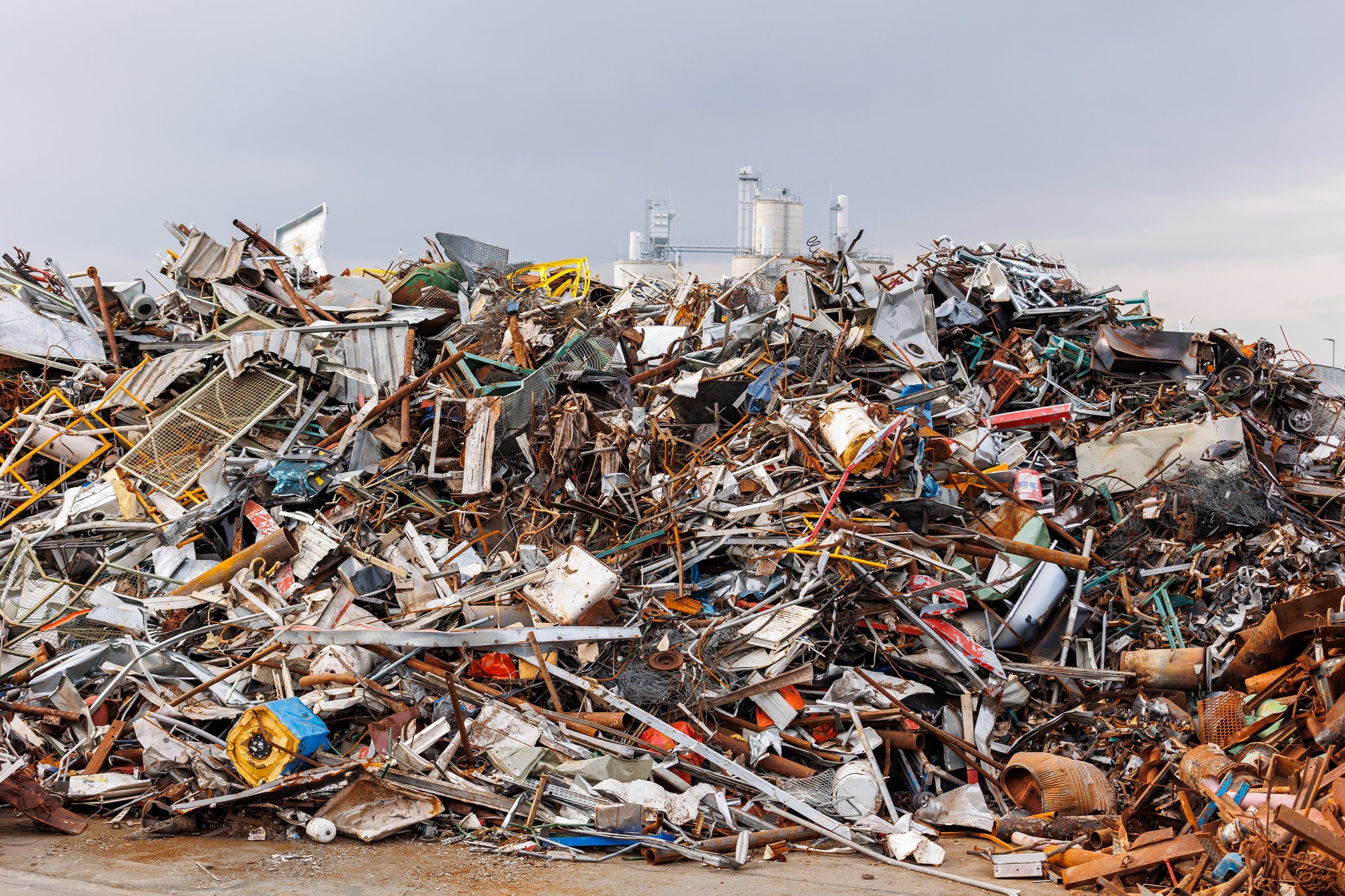 Scenic metal scrap yard huge pile of rusty metal parts disposal waste at junkyard recycling site against industrial factory plant area at Germany. Scrapyard waste management industry background.