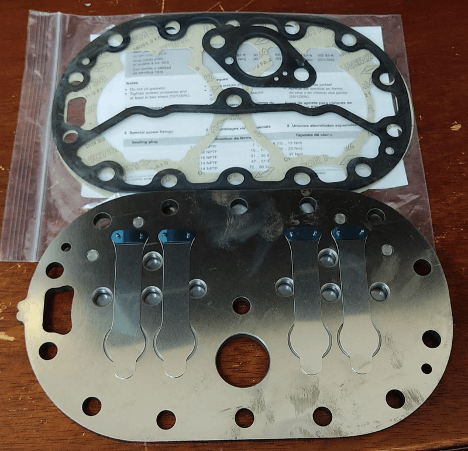 Two metallic gasket plates on a wooden table, one with a black rubber lining and the other with metal flaps.