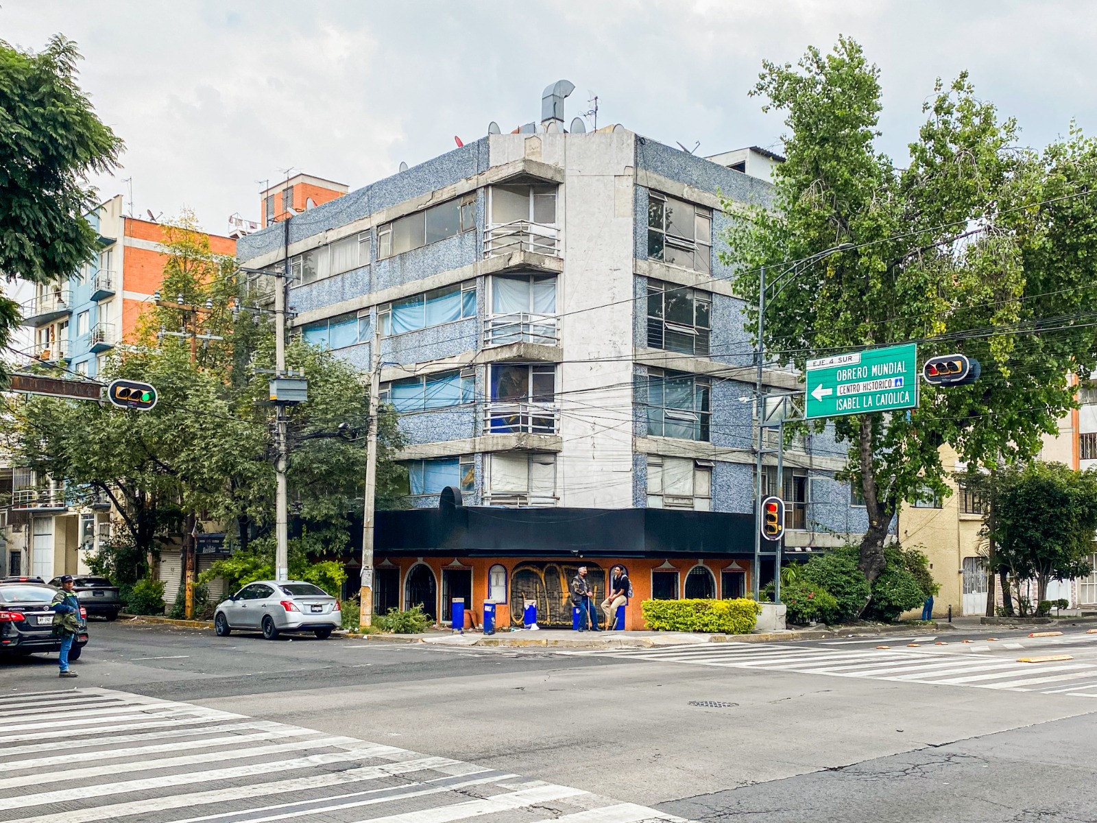 Street corner with a blue-gray building, traffic lights, and cars at an intersection in an urban setting.