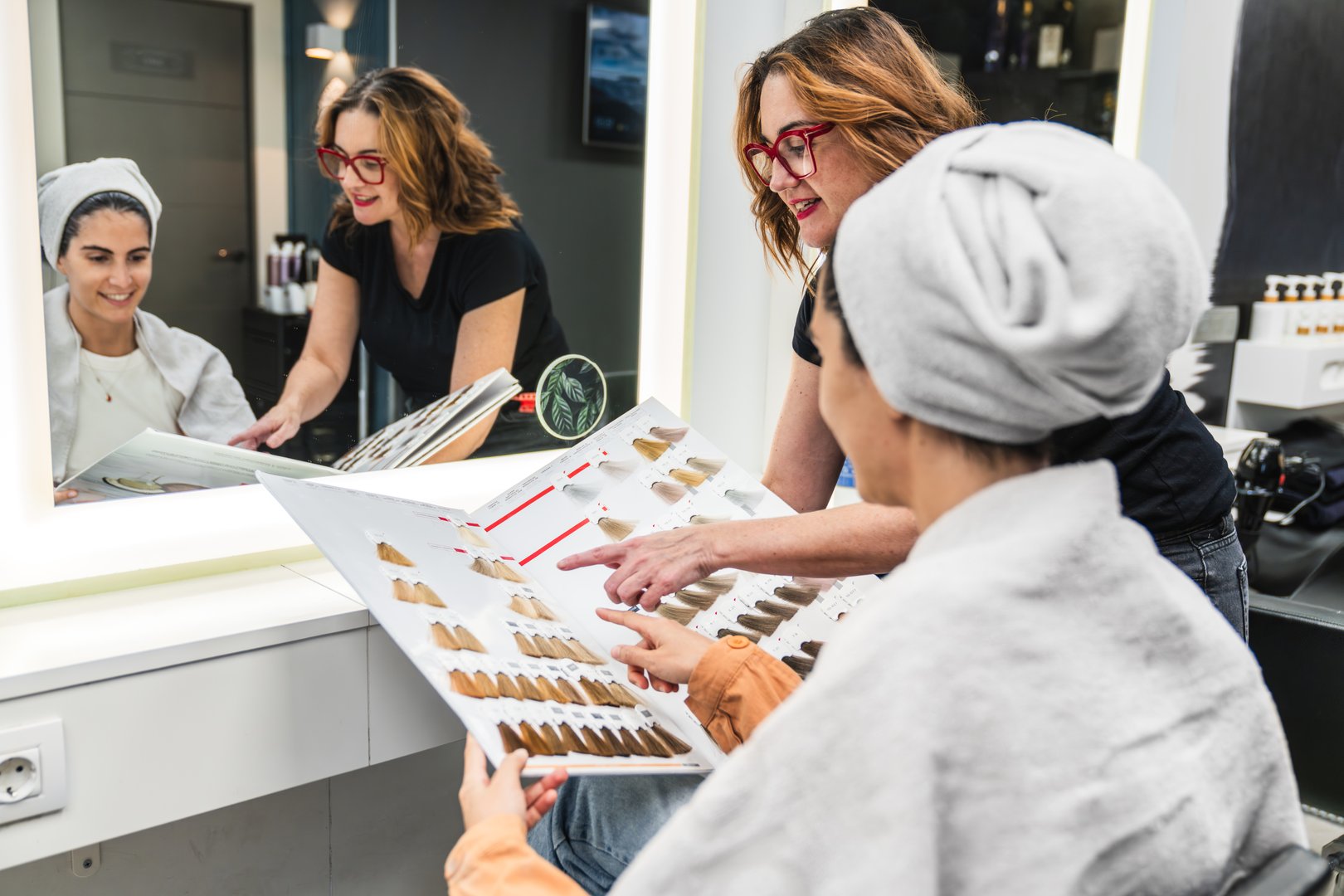 Stylist and client compare hair dye swatches in a bright modern salon, smiling during a professional color consultation and decision making