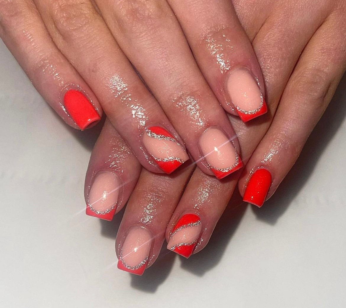 Hands with red and pink manicure featuring silver glitter accents and geometric designs on square-shaped nails.